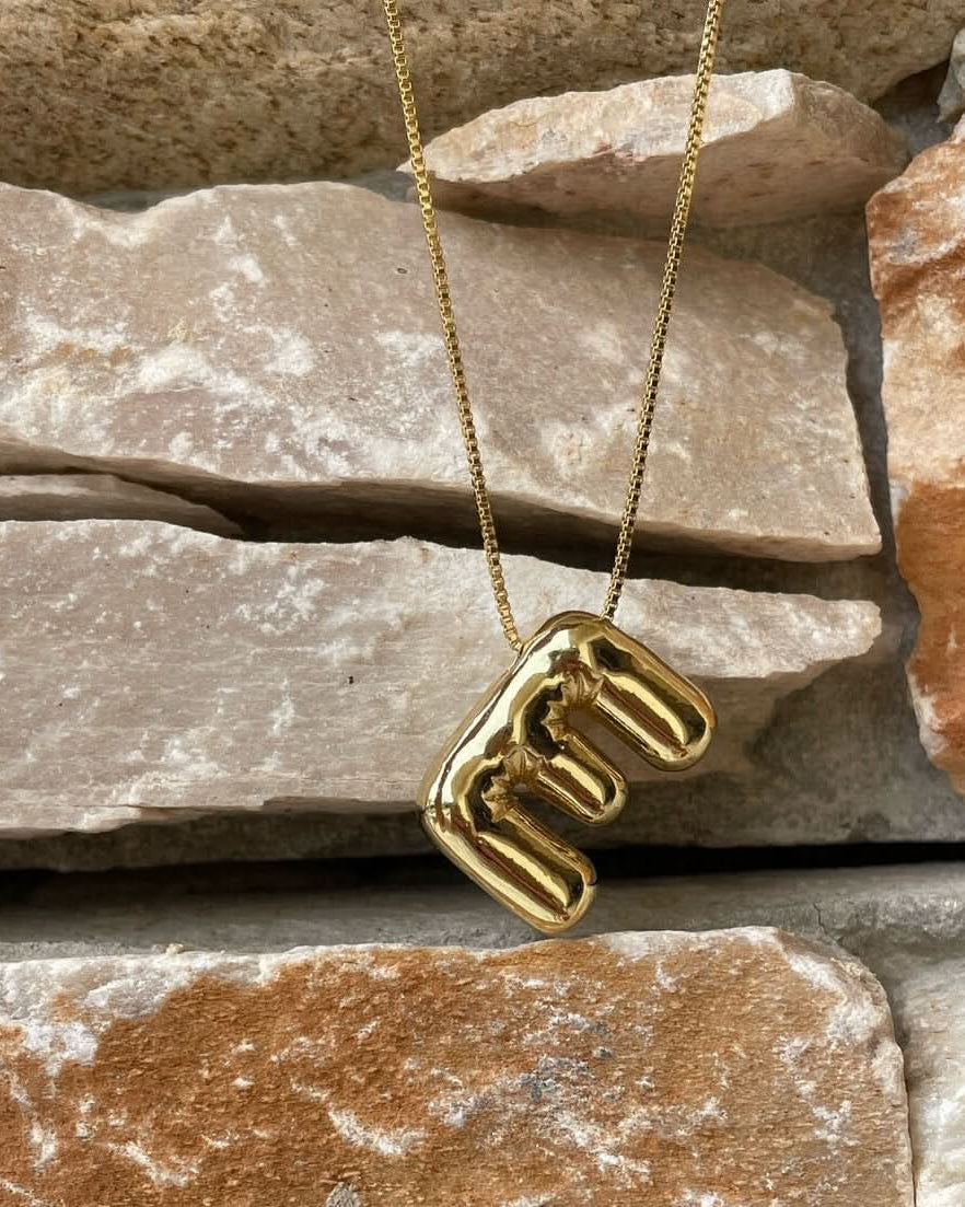 Gold necklace with a unique E Latter pendant on a stone surface