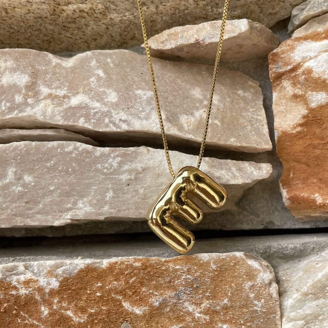 Gold necklace with a unique E Latter pendant on a stone surface