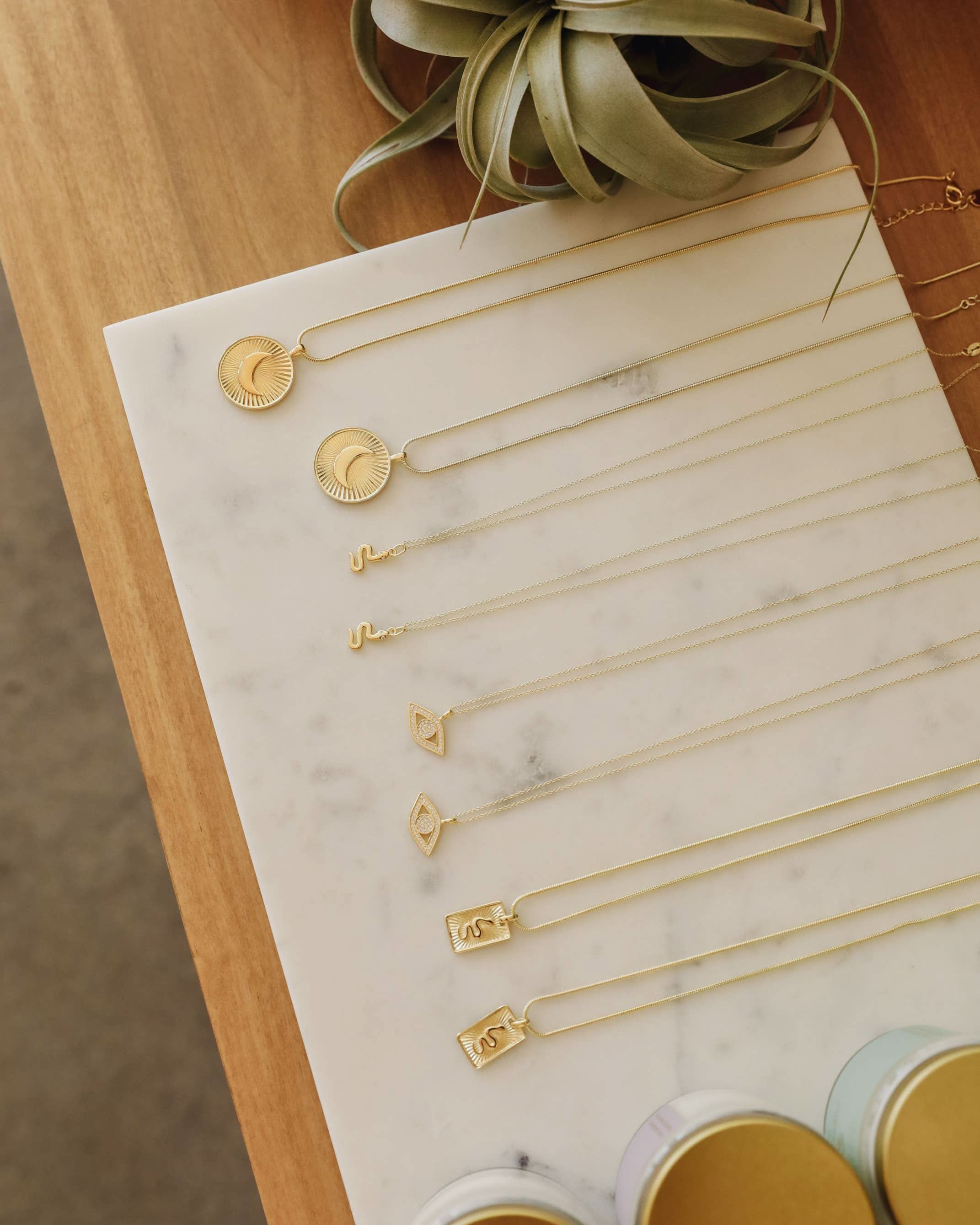 Gold necklaces displayed on a marble surface with a plant in the background