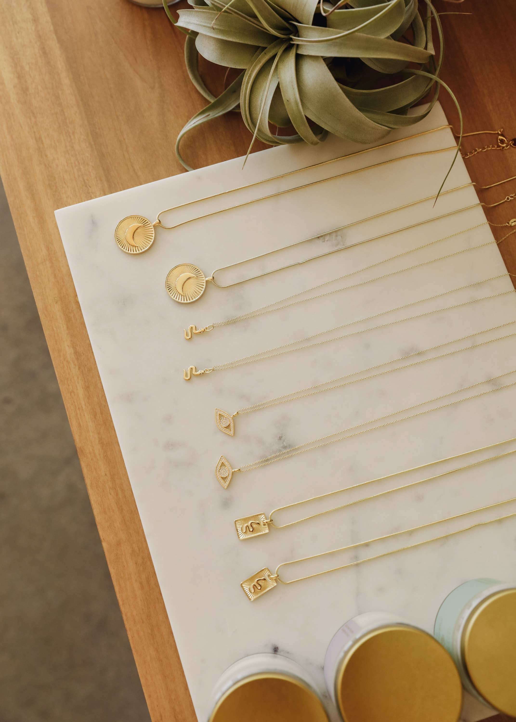 Gold necklaces displayed on a marble surface with a plant in the background