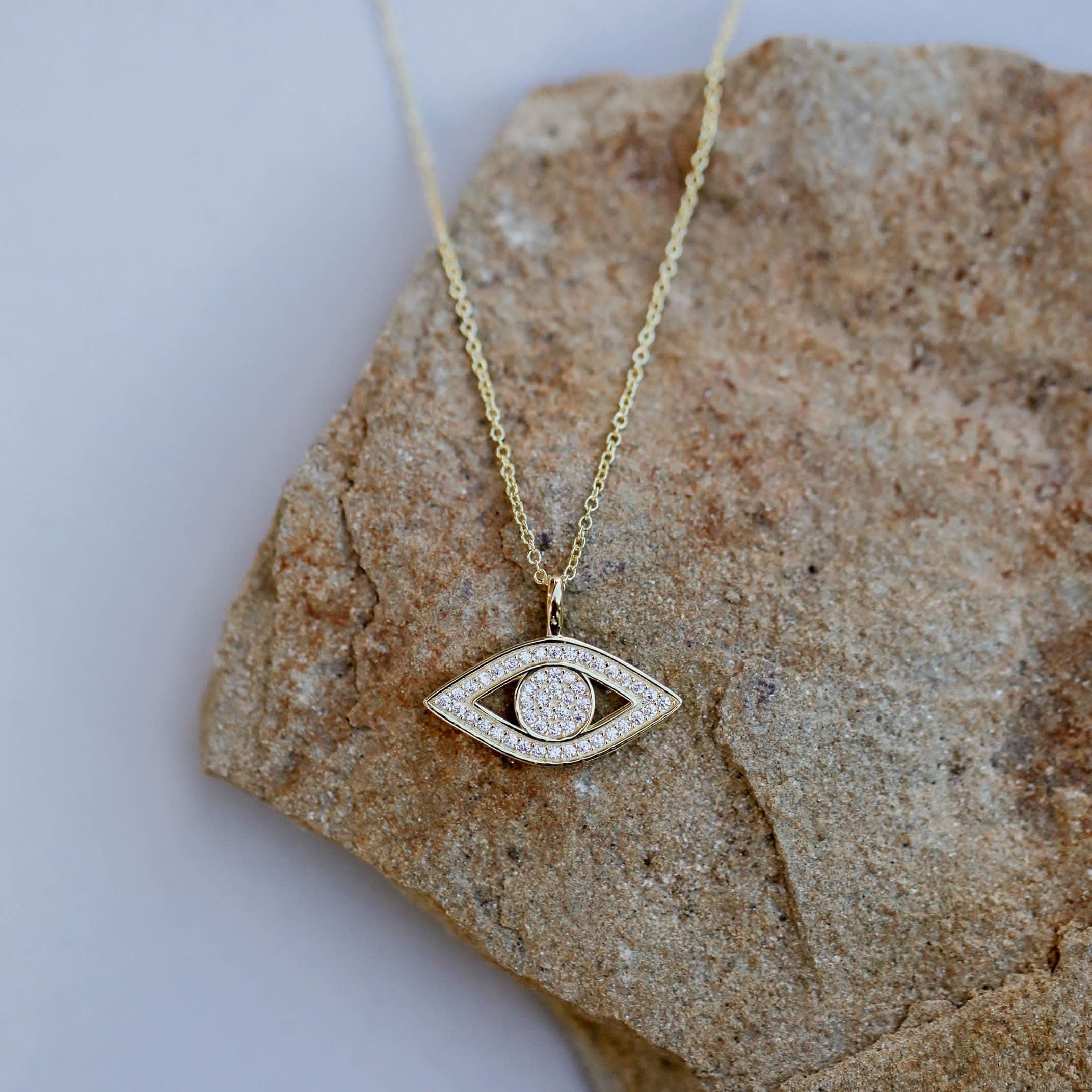 Gold necklace with an eye-shaped pendant on a stone surface