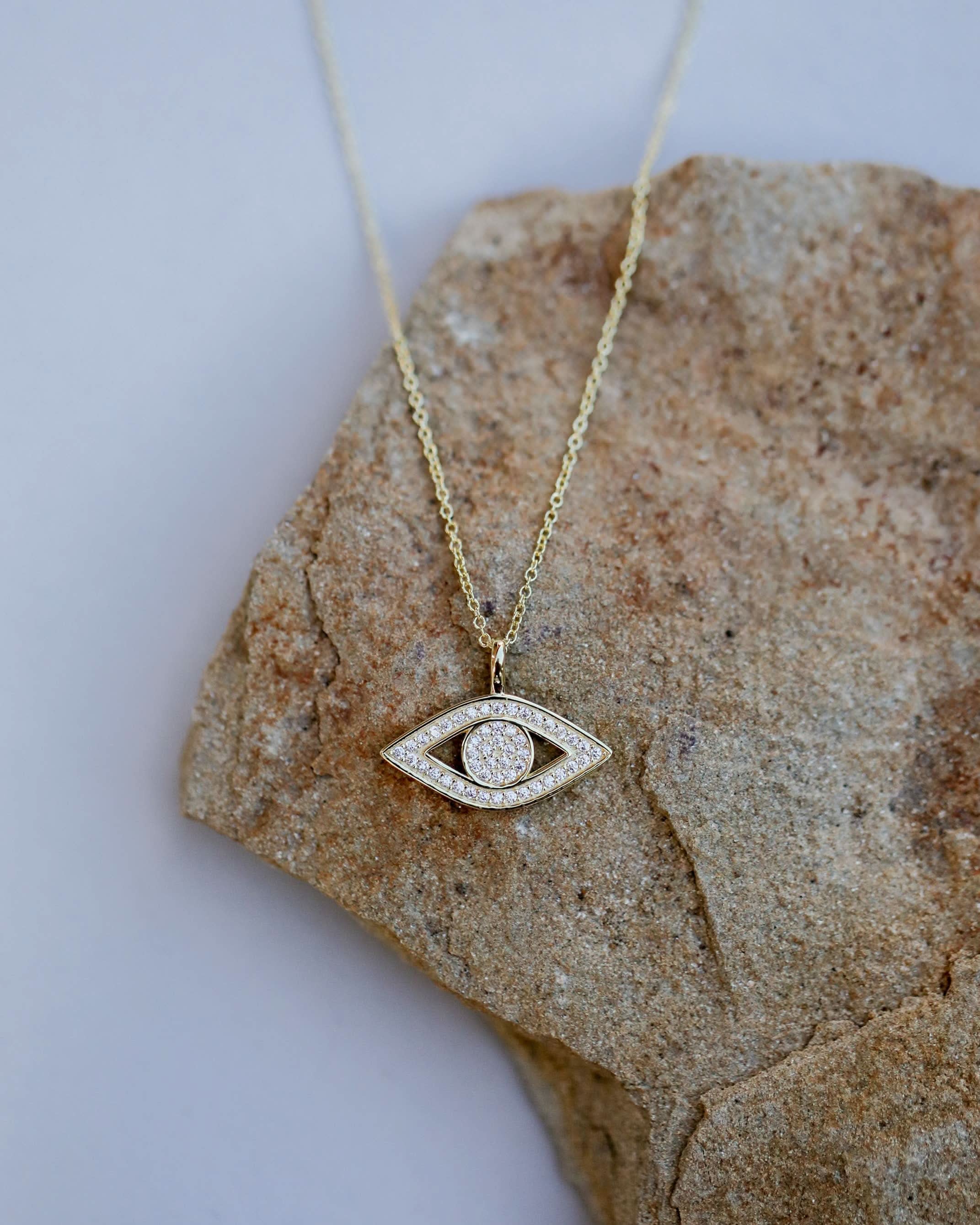 Gold necklace with an eye-shaped pendant on a stone surface