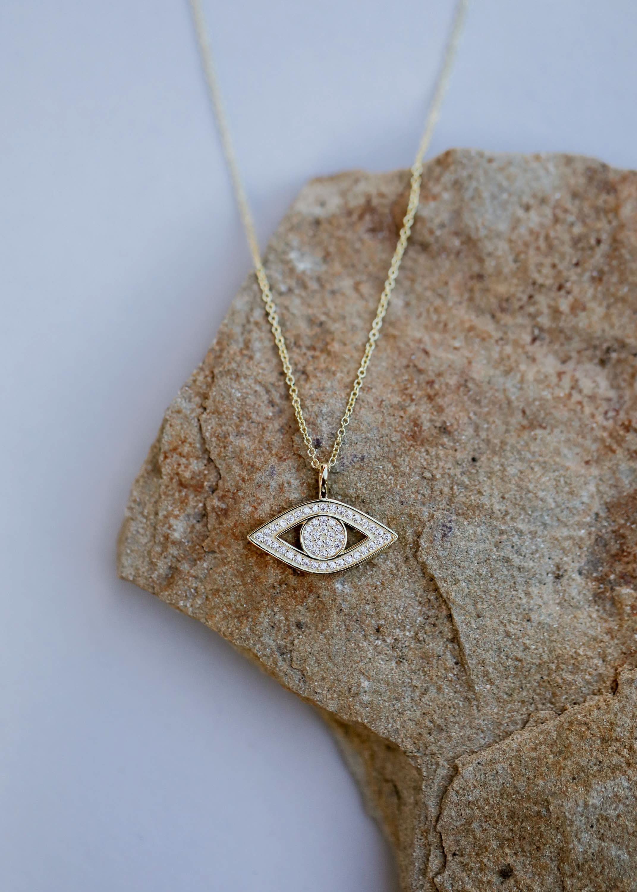 Gold necklace with an eye-shaped pendant on a stone surface