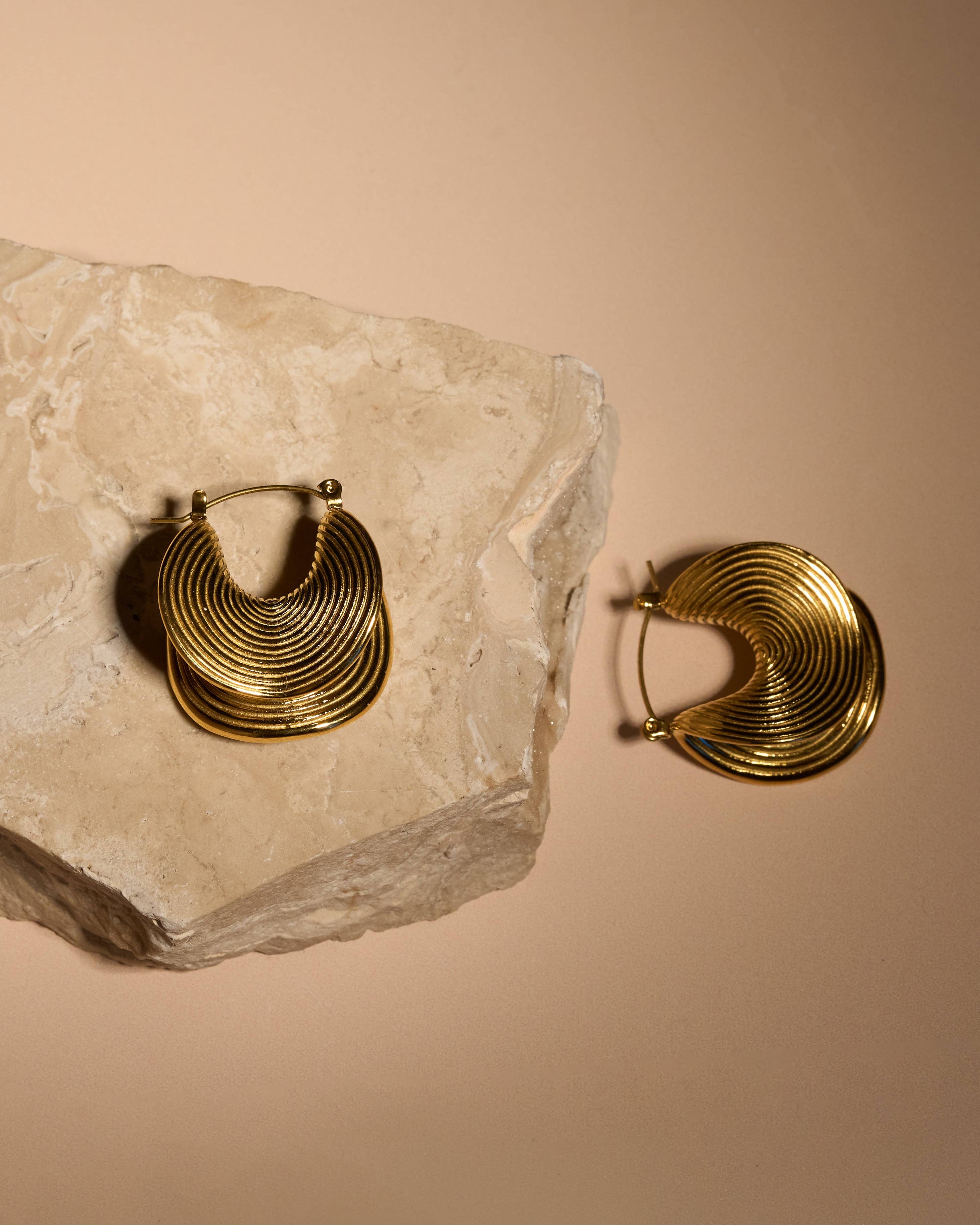Gold hoop earrings on a stone surface with a beige background