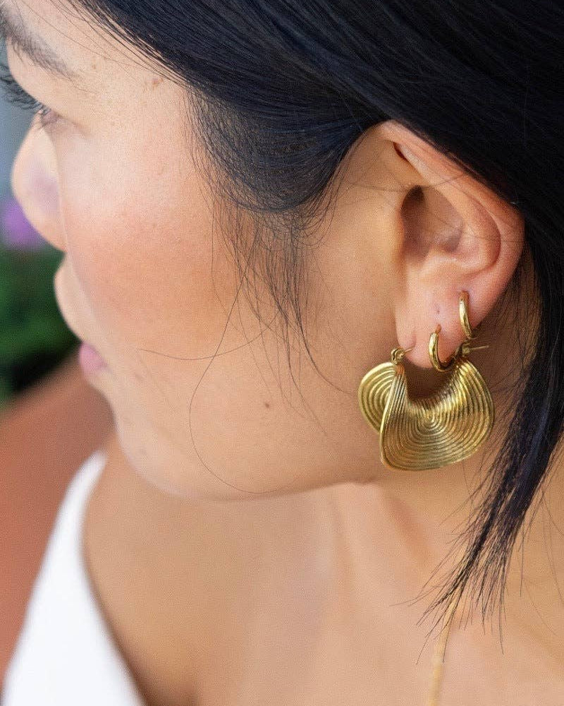Close-up of a person wearing gold hoop earrings with a blurred background