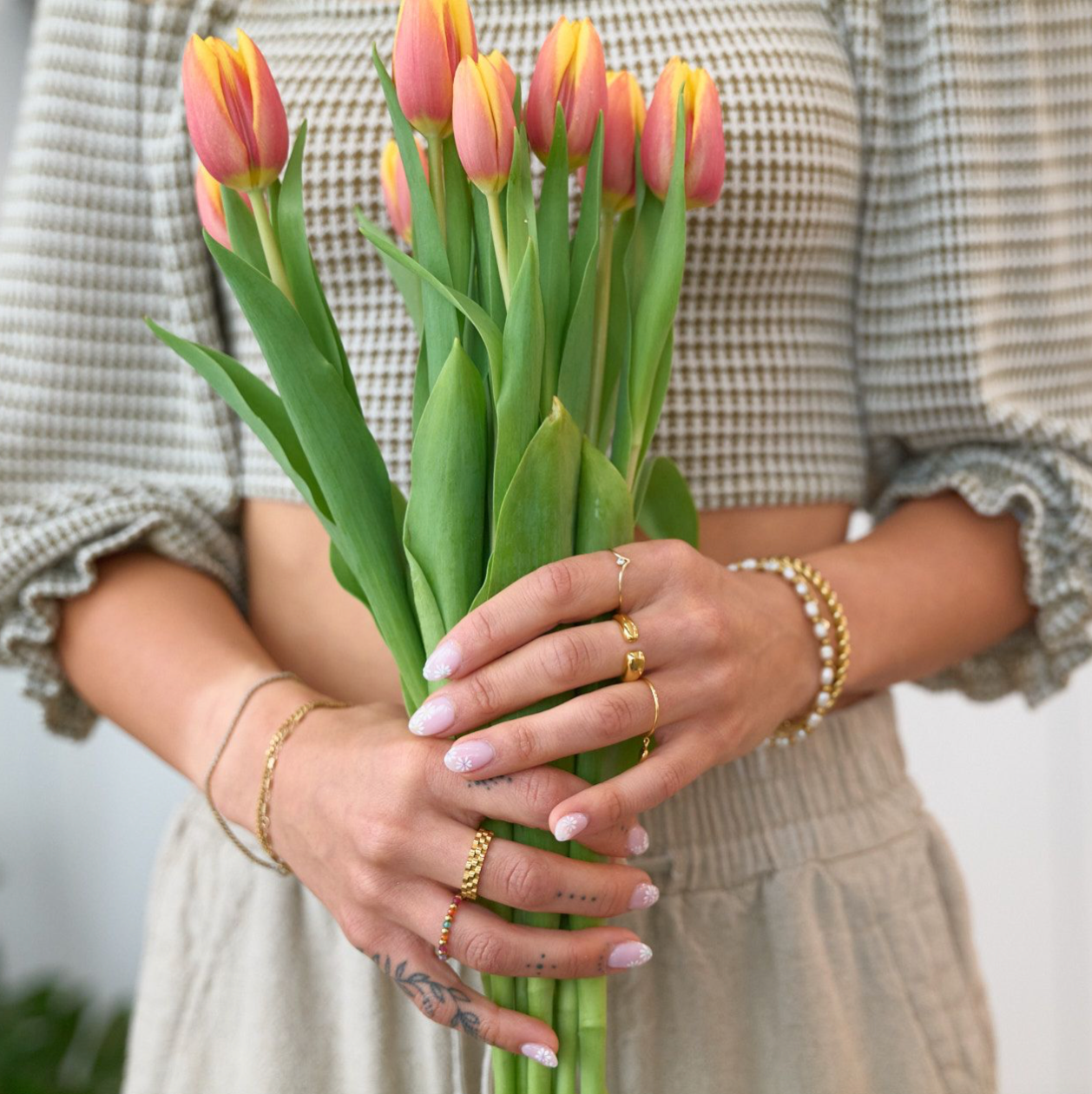 Woman holding flower and many rings including Gold, waterproof, tarnish free, watch band ring on a white background