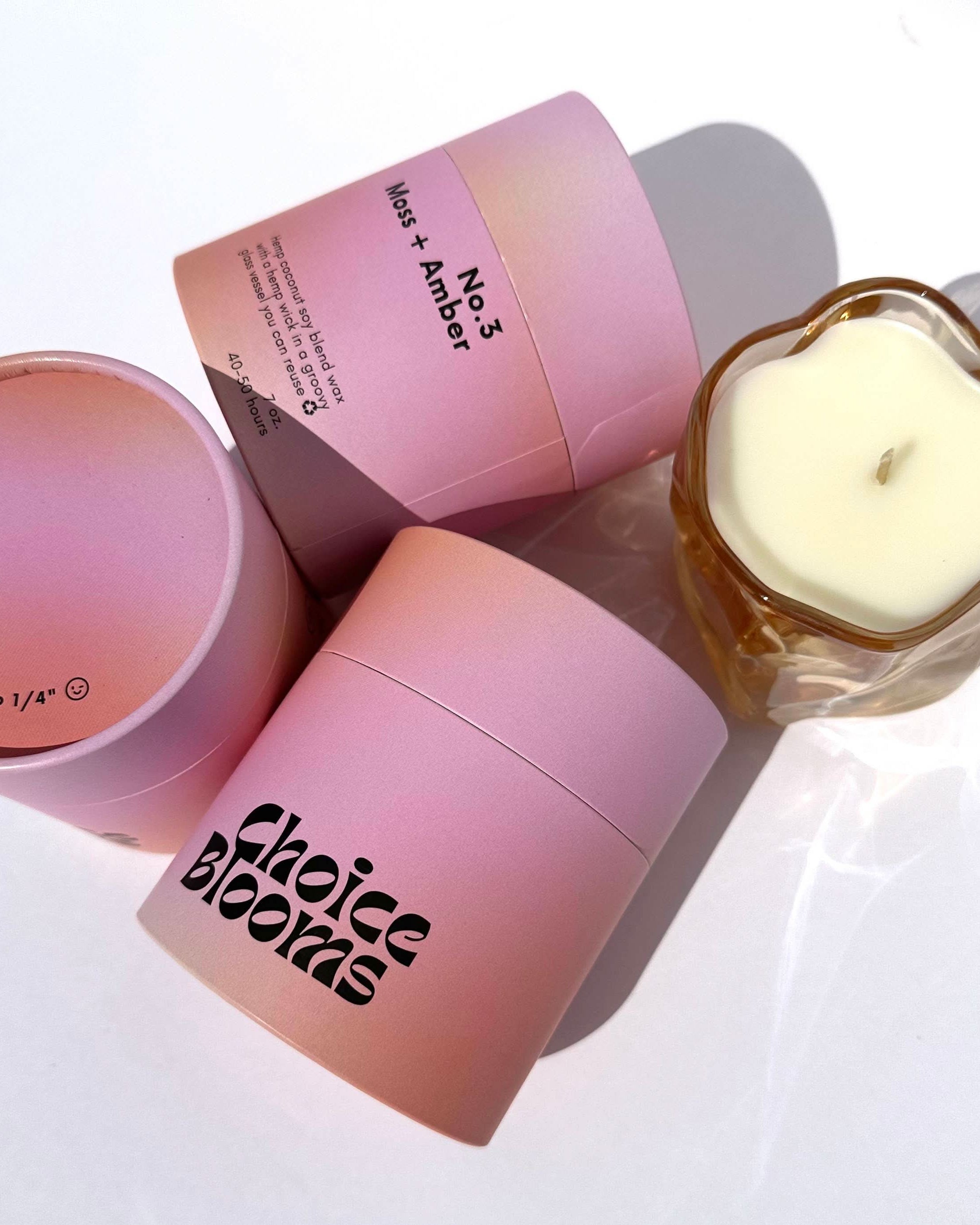 One candle in a pink wavy glass container next to pink 3 candle packaging containers