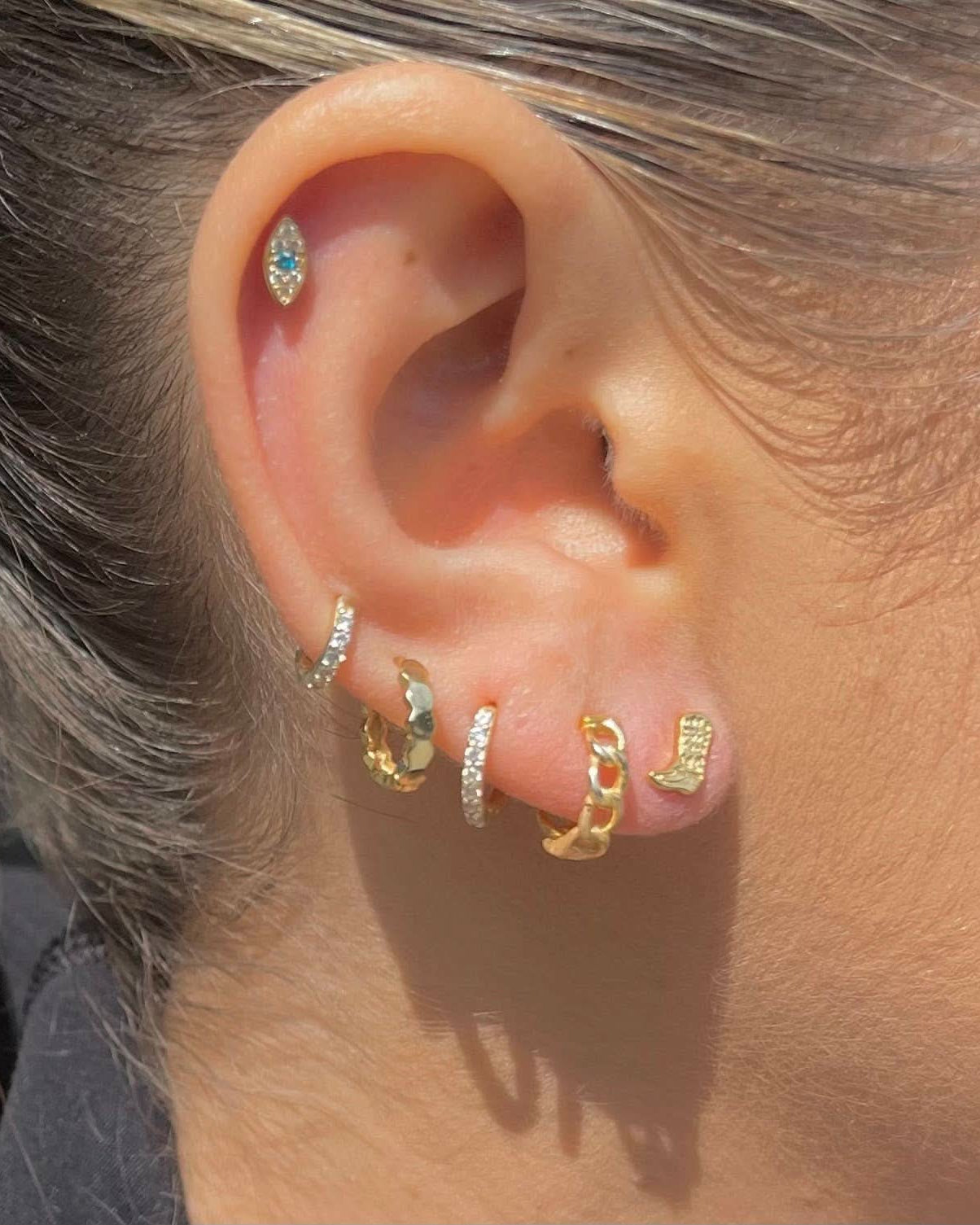Close-up of an ear with multiple gold and silver hoop earrings.