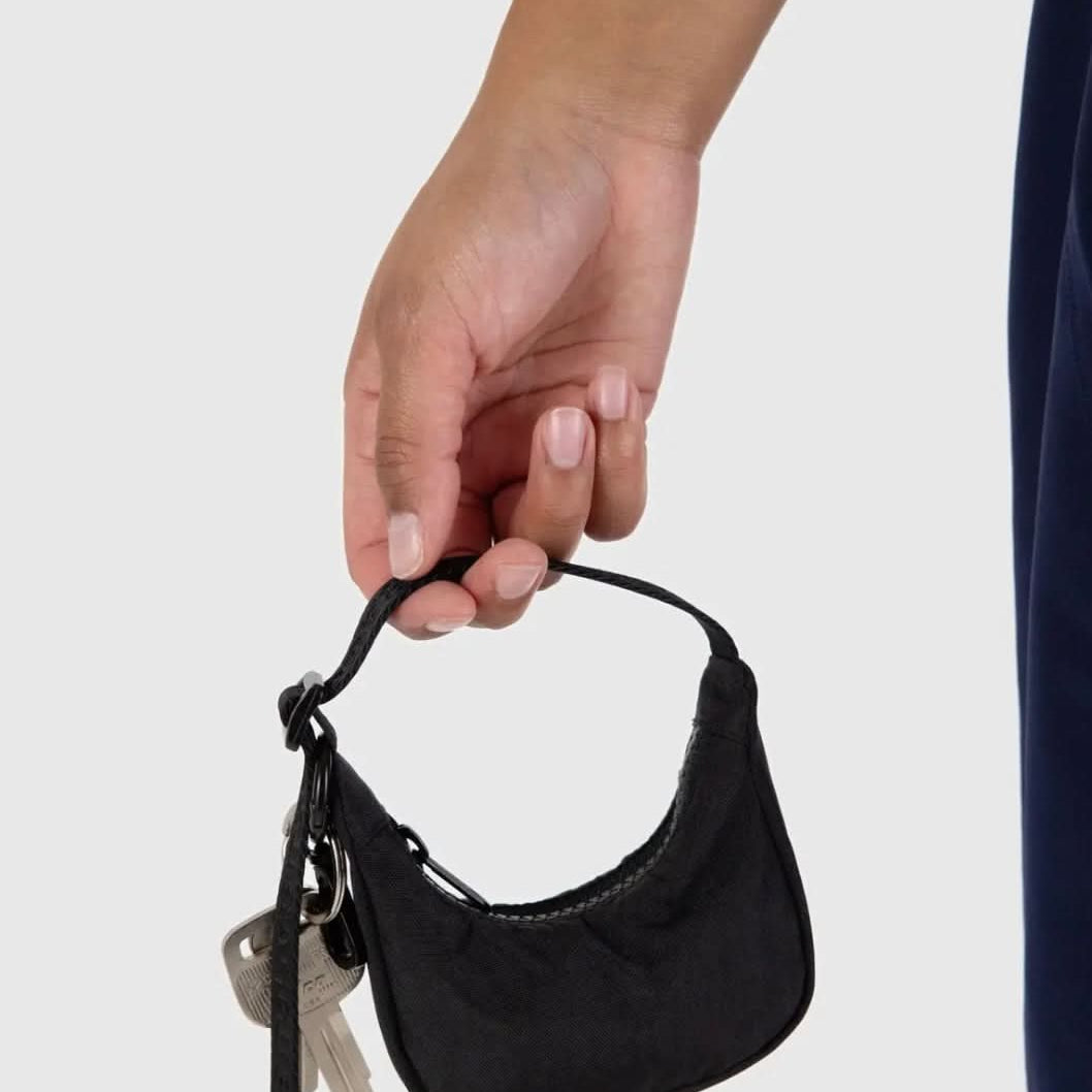Model holding tiny black baby BAGGU bag charm, Fully functional zipper, and keys clipped to the bag