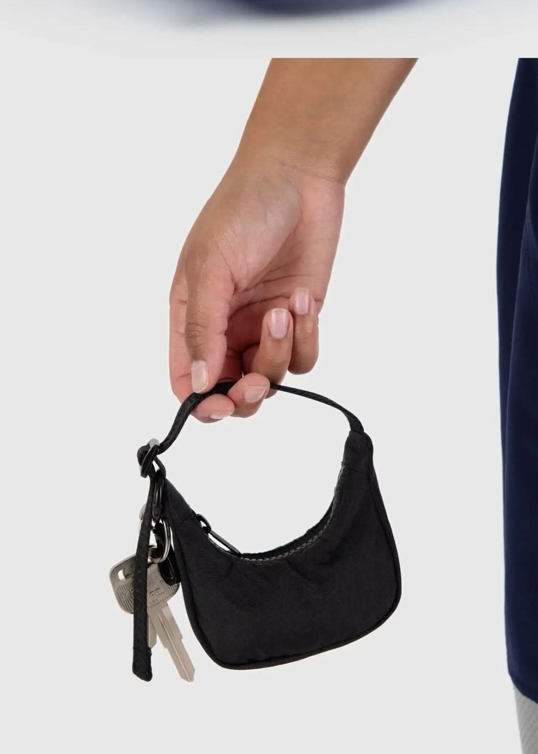 Model holding tiny black baby BAGGU bag charm, Fully functional zipper, and keys clipped to the bag