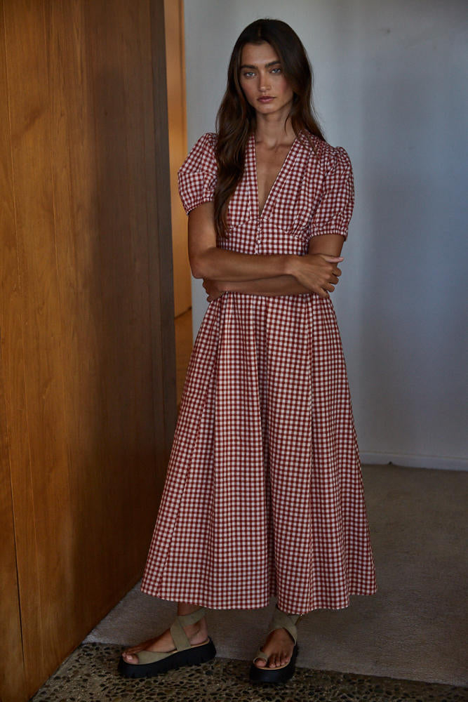 Woman wearing a red and white checkered dress standing against a wooden wall.