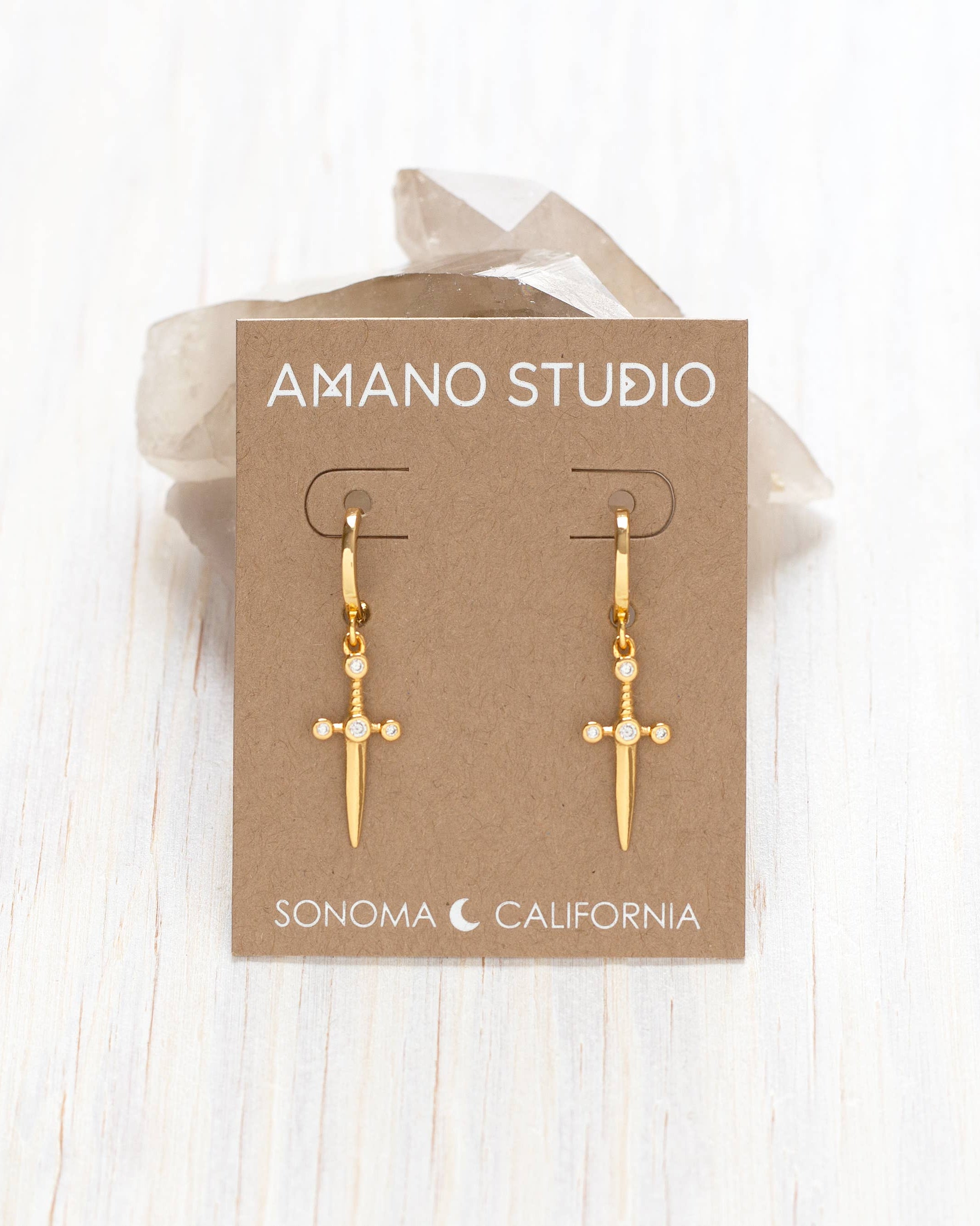 Gold earrings on a 'Amano Studio' branded card with a white background