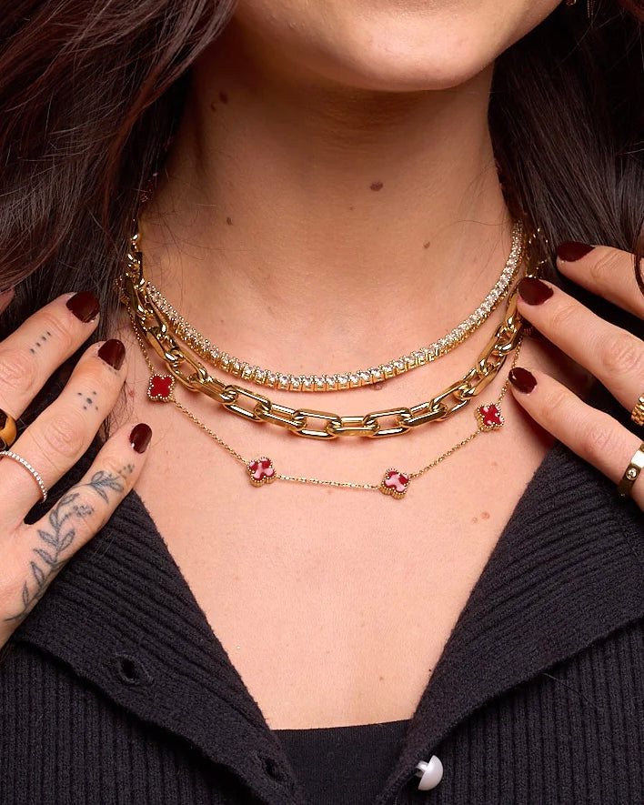 Close-up of a person wearing multiple gold necklaces with red pendants.