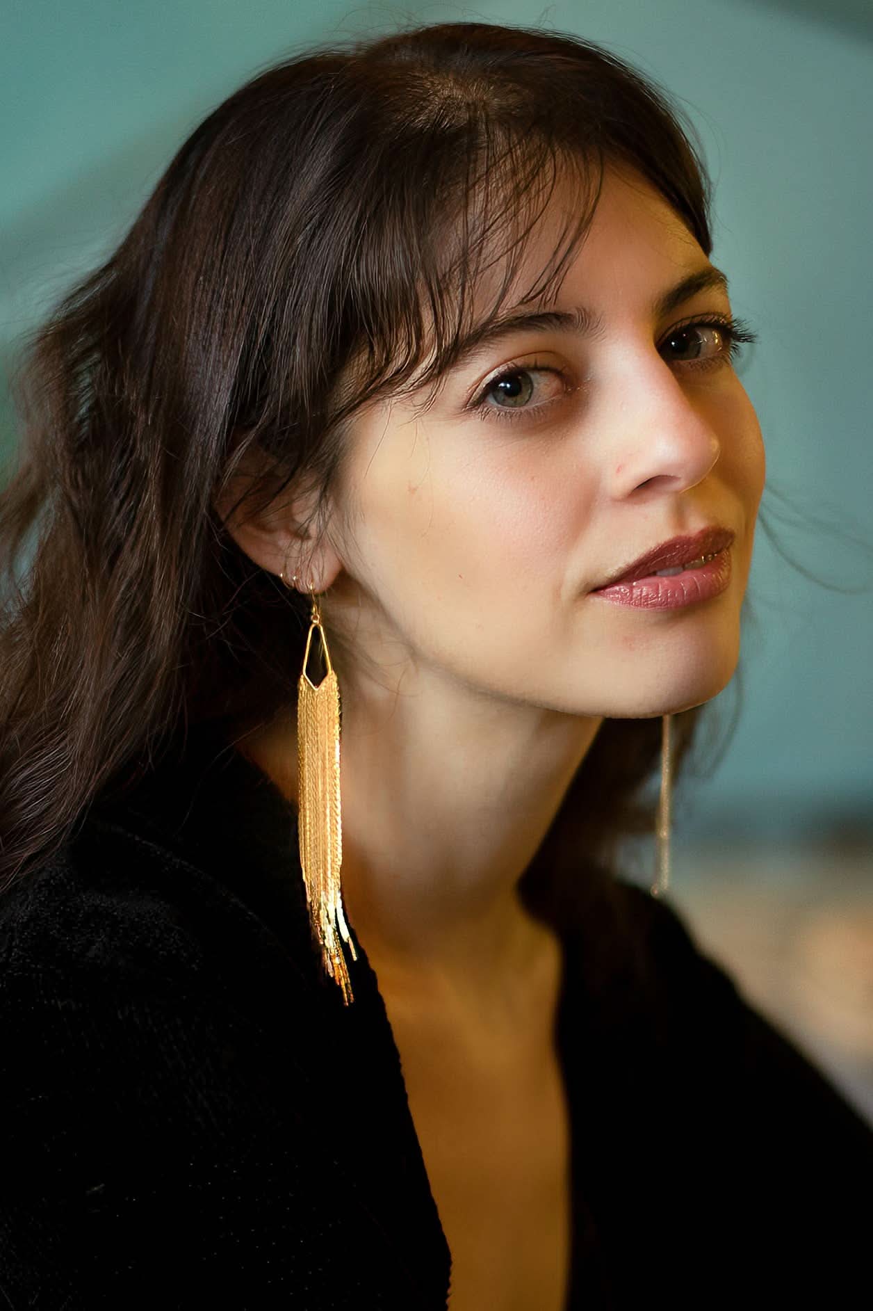 Woman wearing long gold earrings against a blurred background