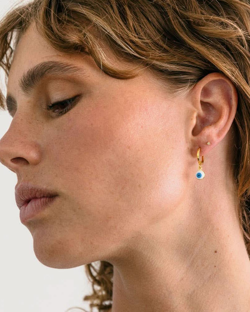 Woman wearing Gold earring with glass evil eye charm white with blue eye