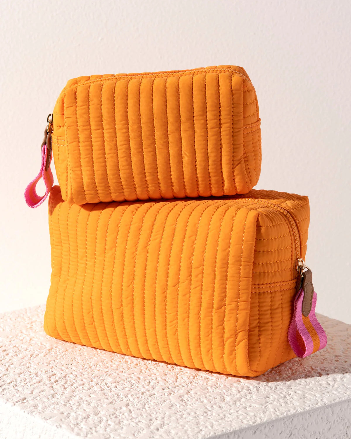 Two orange quilted pouches with pink zippers on a textured surface.