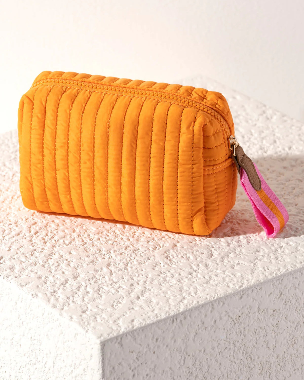 Orange quilted cosmetic bag with a pink strap on a textured surface