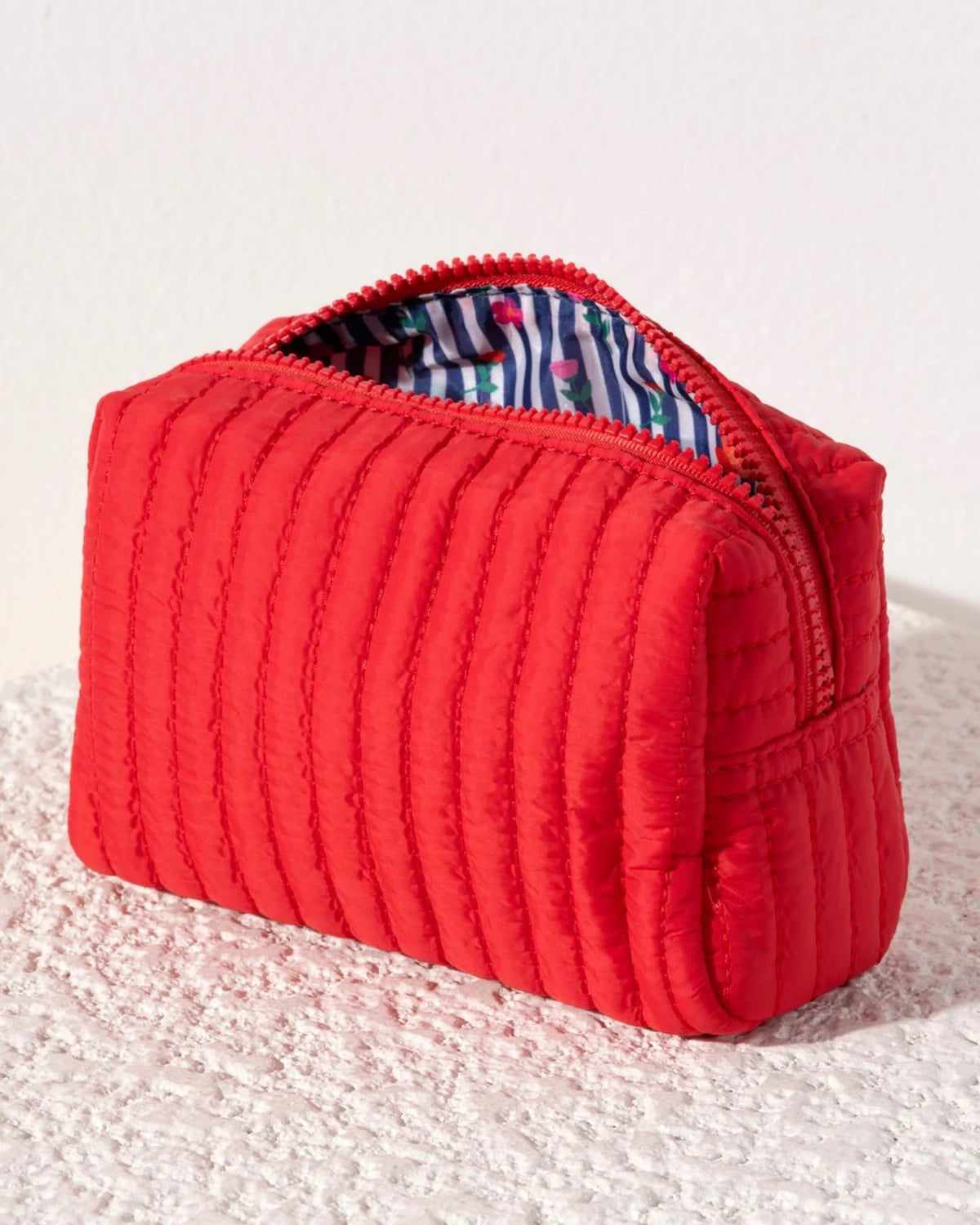 Ezra small boxy cosmetic pouch Red quilted pouch on a textured white surface