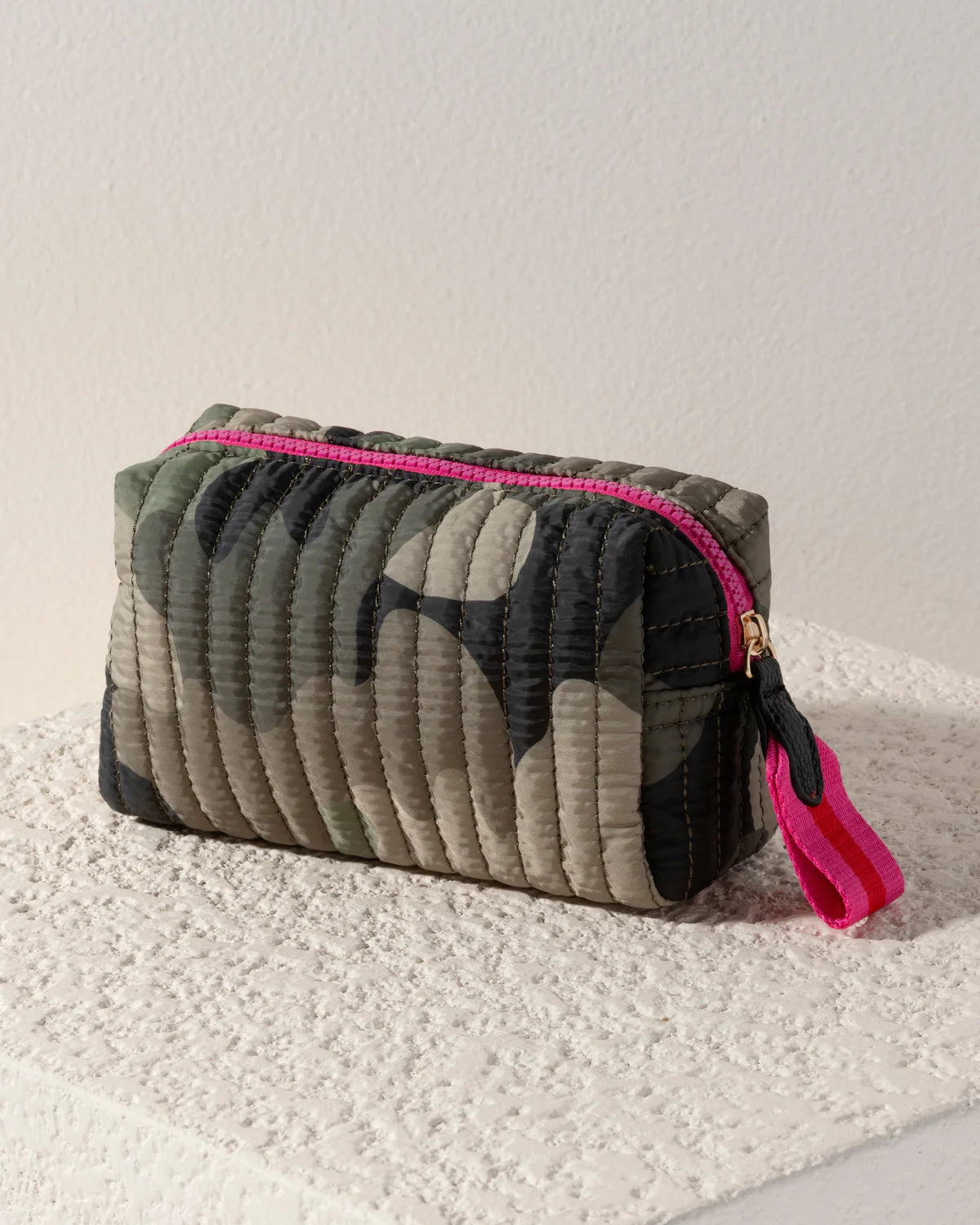Camouflage-patterned pouch with pink zipper and tassel on a light surface