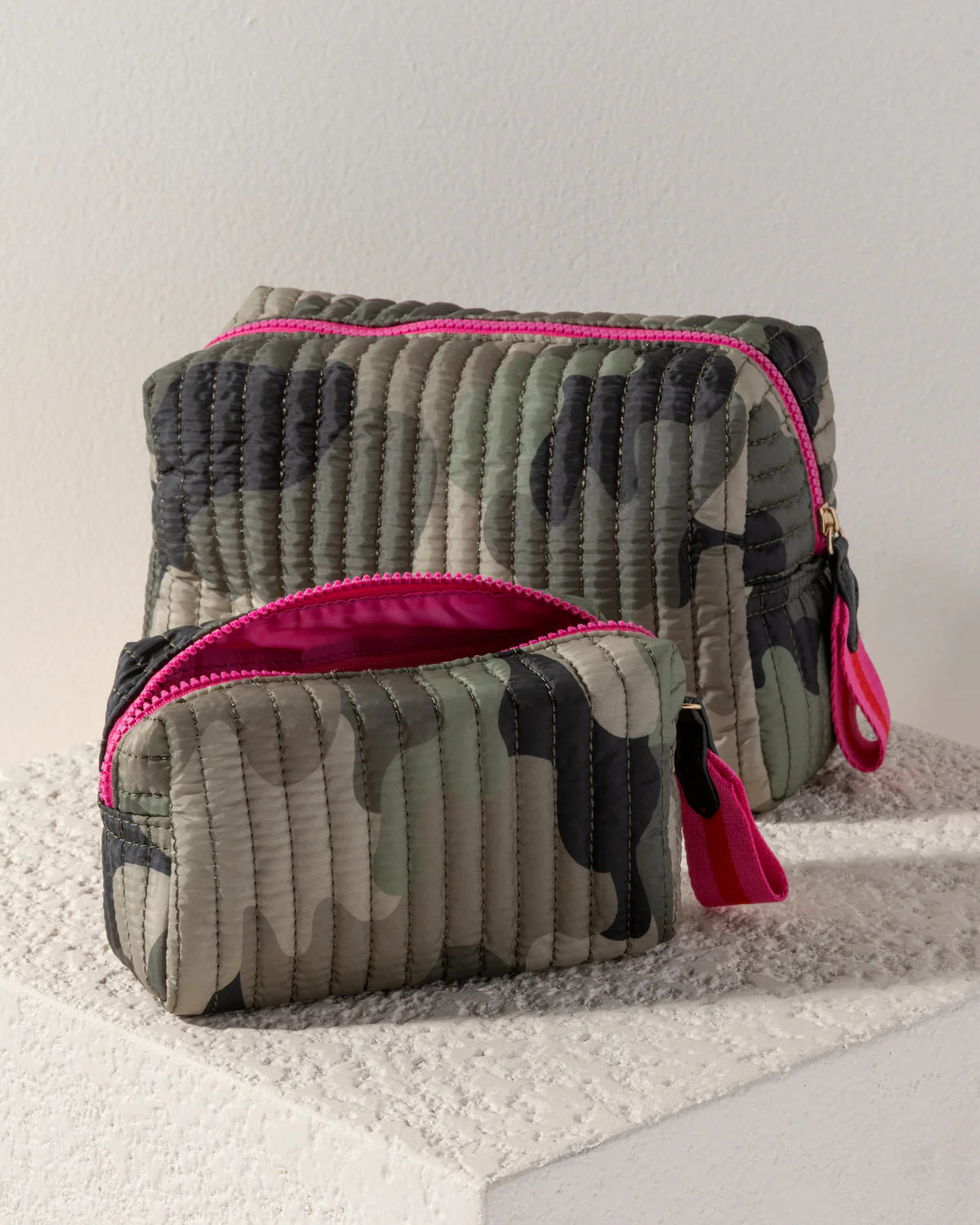 Two camouflage-patterned pouches with pink zippers on a textured surface.