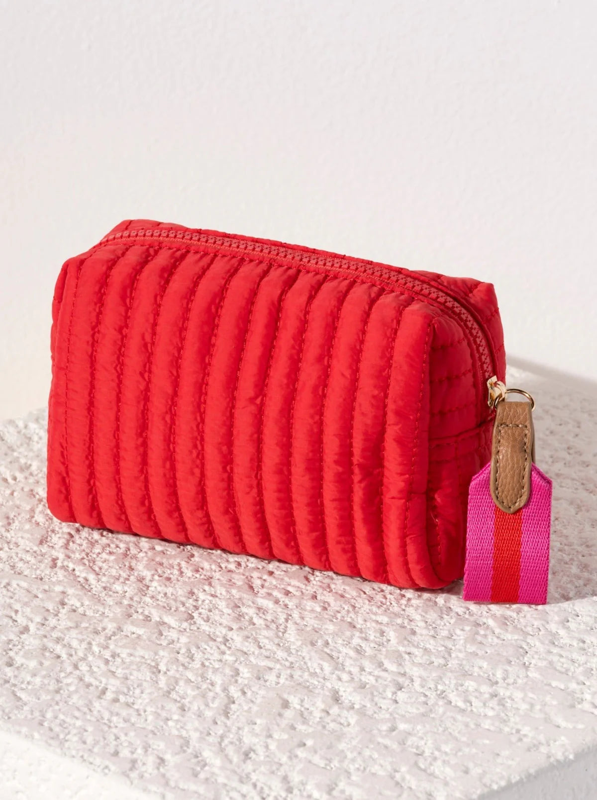 Red textured pouch with a pink strap on a textured white surface