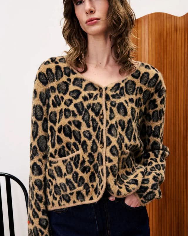 Person wearing a leopard print cardigan in front of a wooden door.