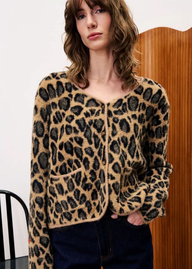 Person wearing a leopard print cardigan in front of a wooden door.