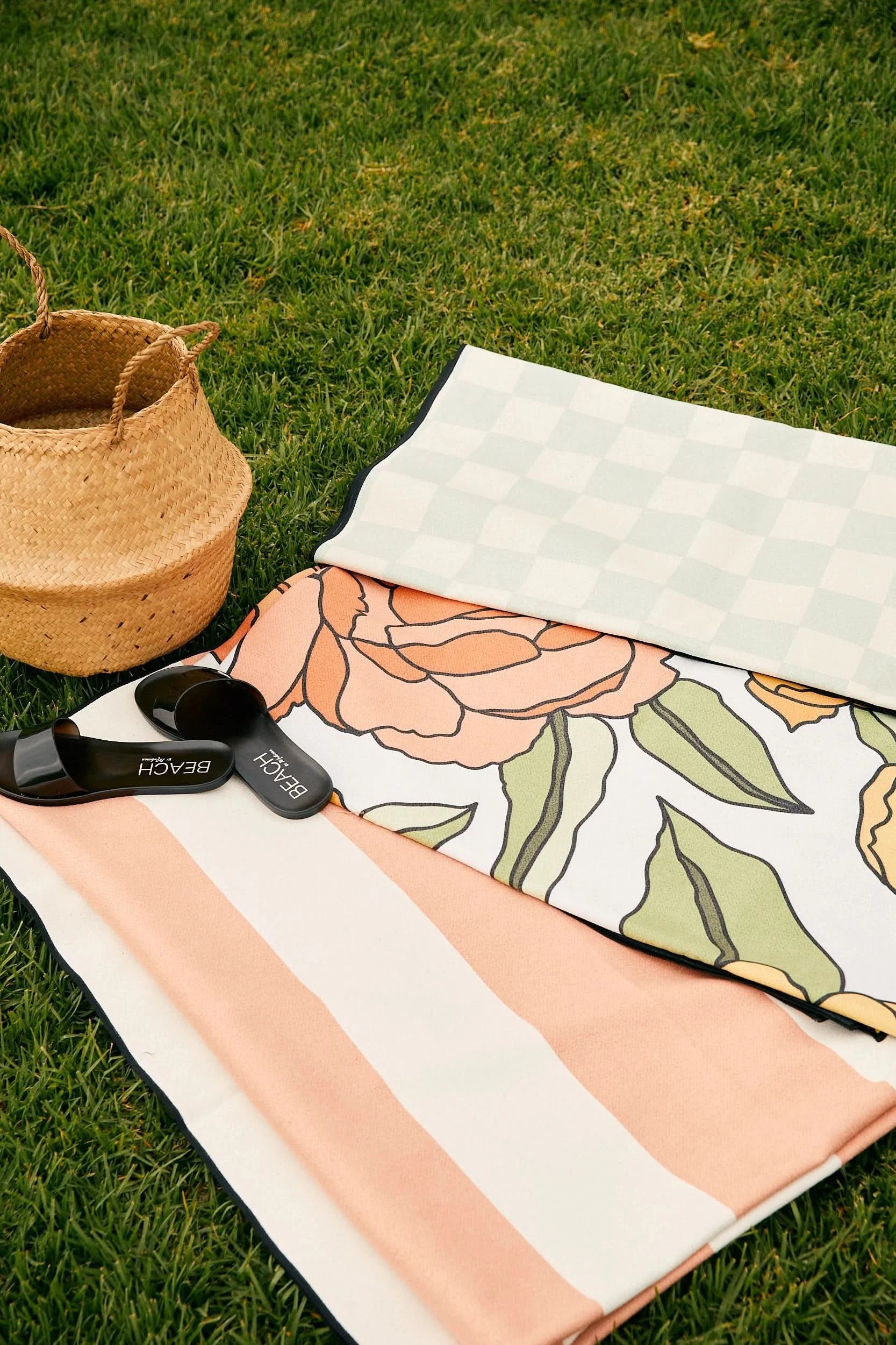 Floral-patterned towel on grass with a basket and sandals