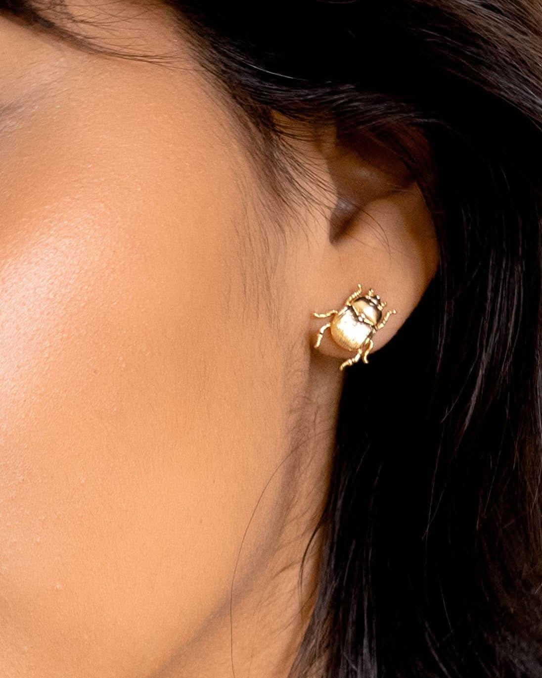 Close-up of a person wearing a gold earring with a gemstone.