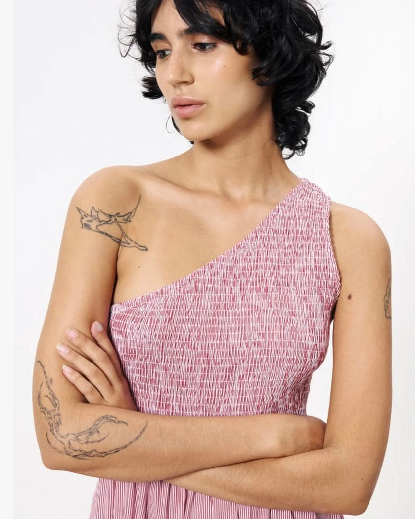 Woman wearing a pink one-shoulder dress with tattoos on her arms