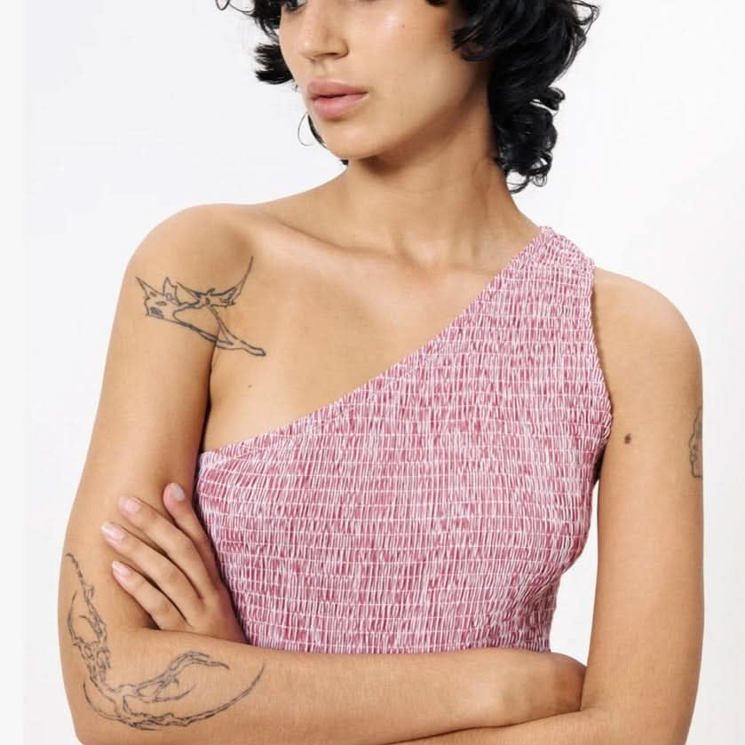 Woman wearing a pink one-shoulder dress with tattoos on her arms