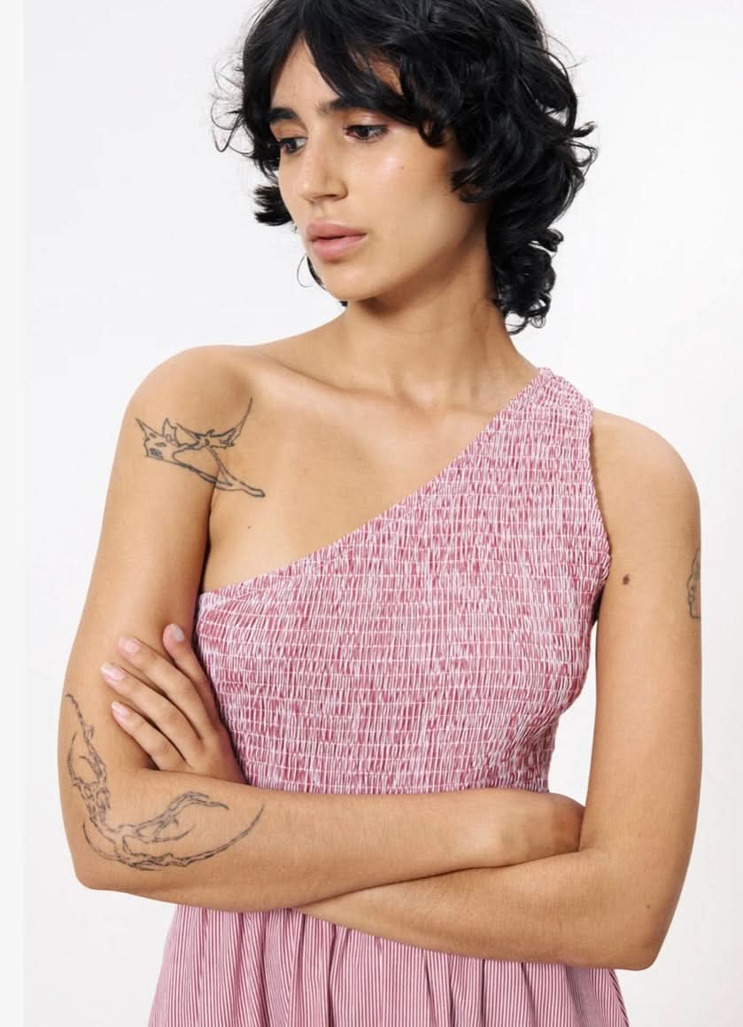 Woman wearing a pink one-shoulder dress with tattoos on her arms