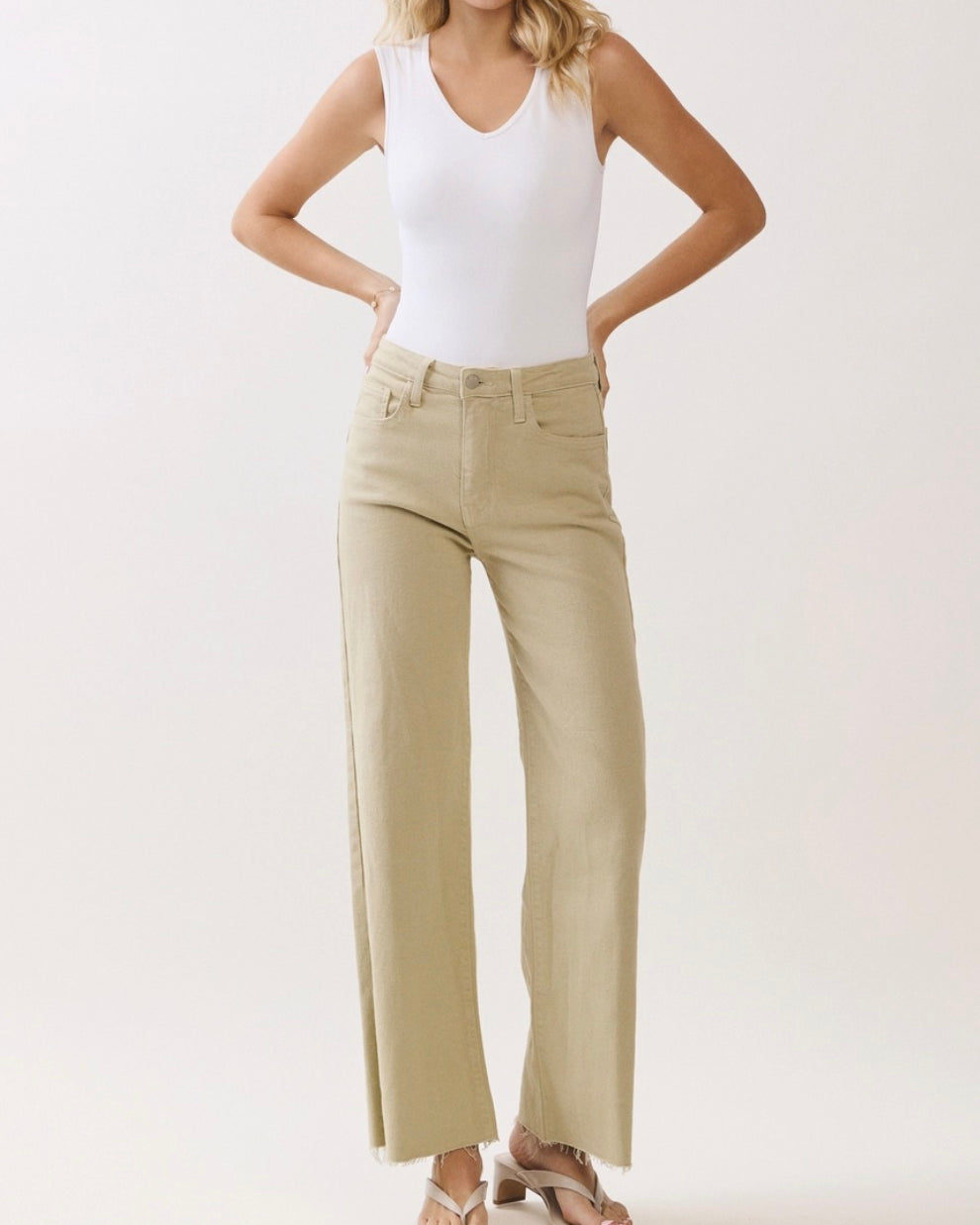 Woman wearing a white tank top and beige wide-leg pants on a light background