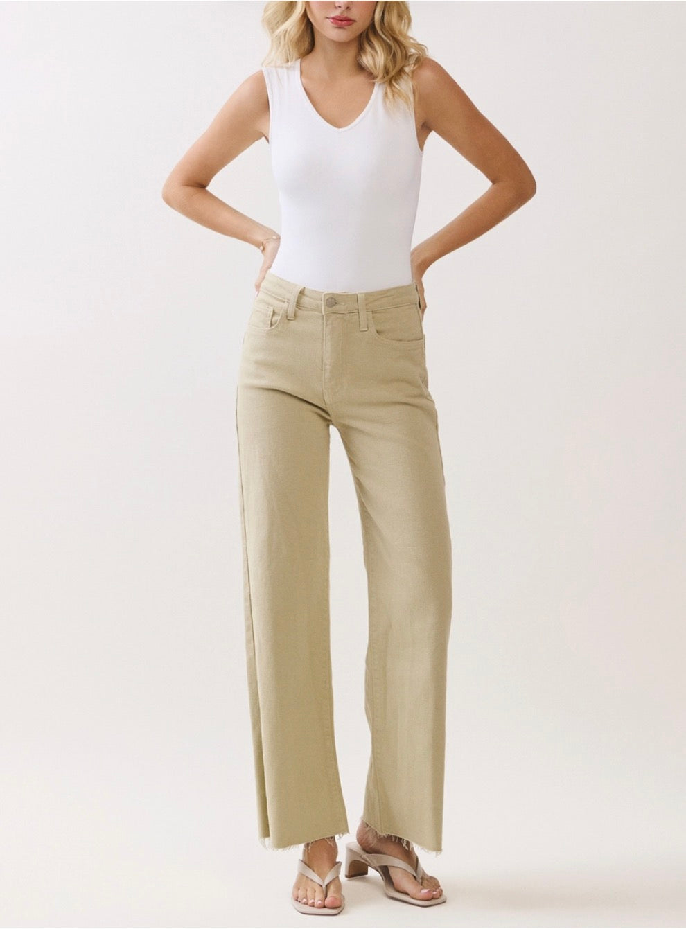 Woman wearing a white tank top and beige wide-leg pants on a light background