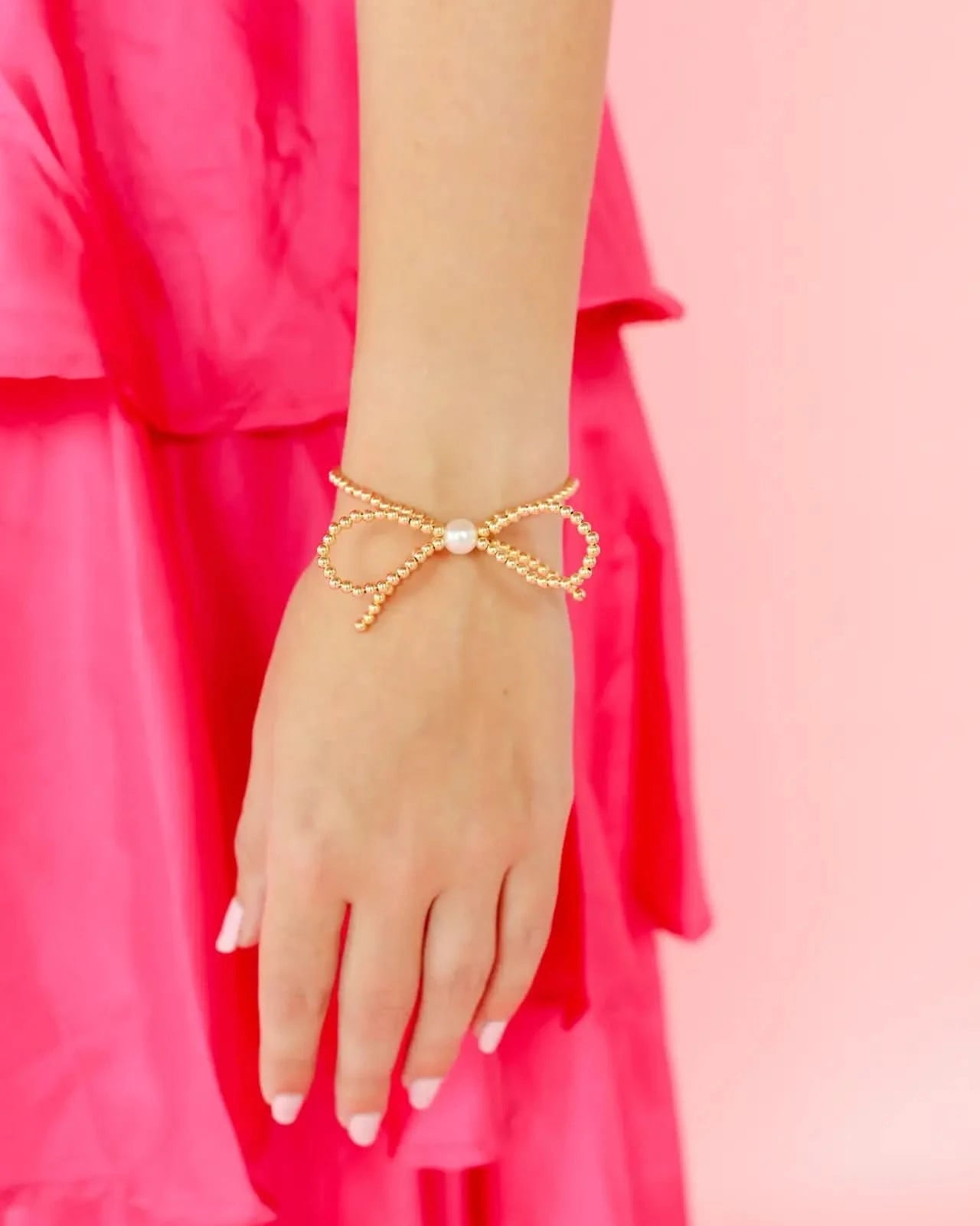 Gold bracelet with a pearl on a hand against a pink background