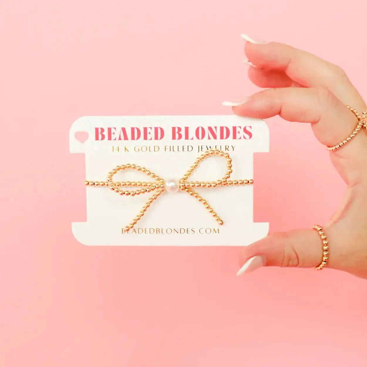 Gold hair tie on a 'Beaded Blondes' card against a pink background