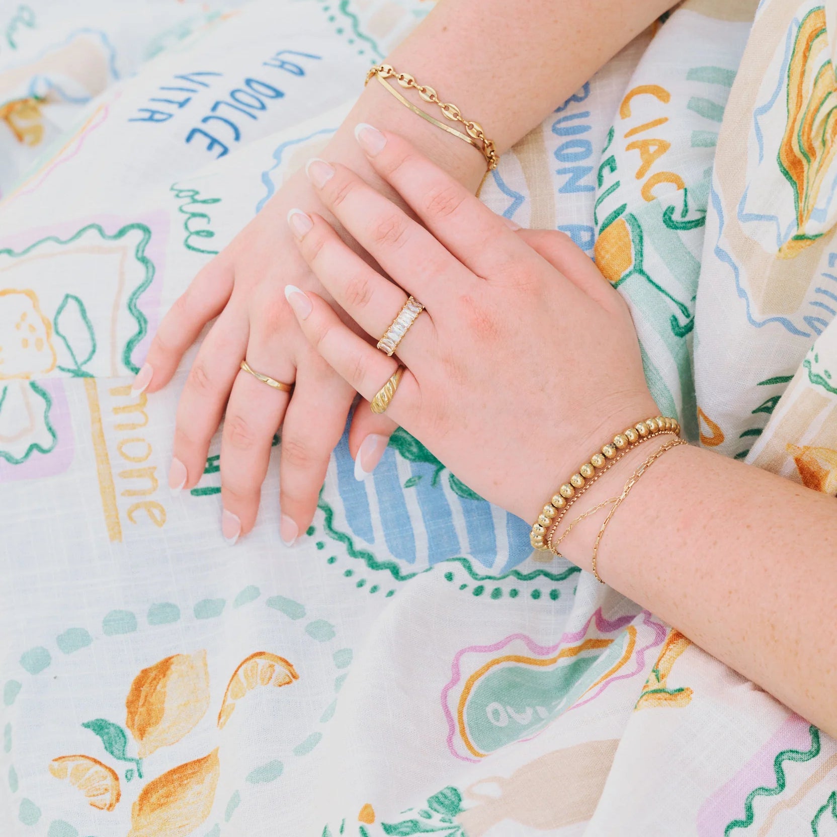 Close-up of hands with rings included golden croissant Ring on a patterned fabric background