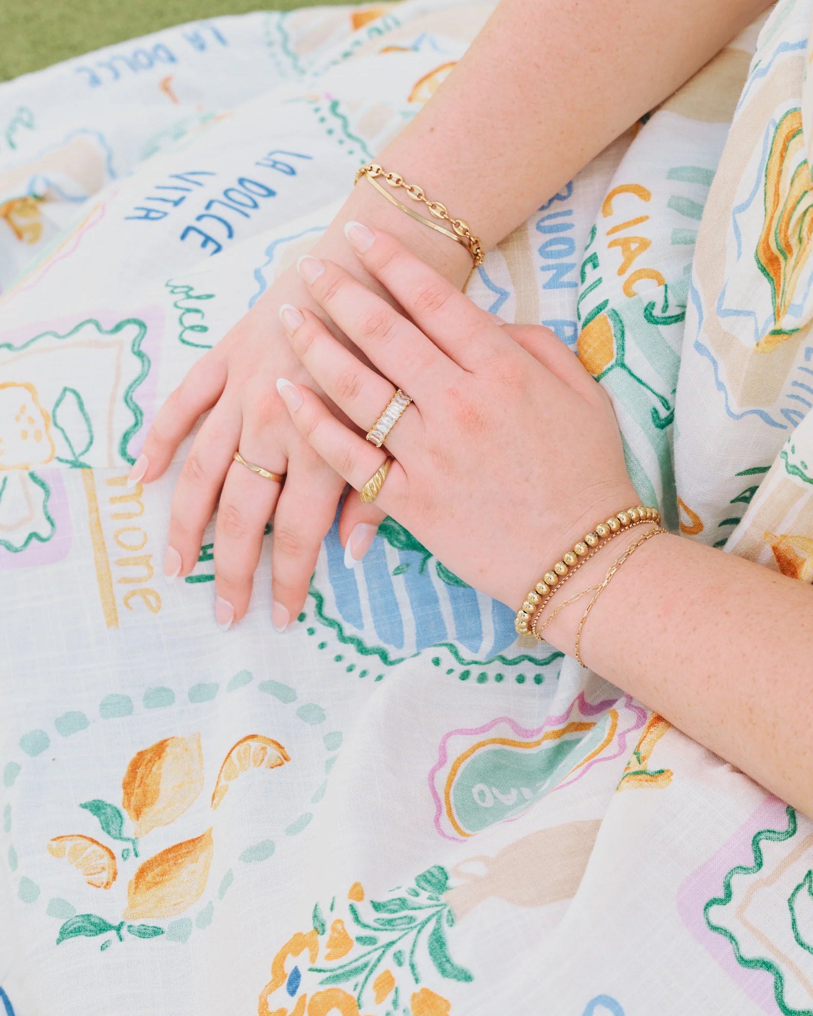 Close-up of hands with rings included golden croissant Ring on a patterned fabric background