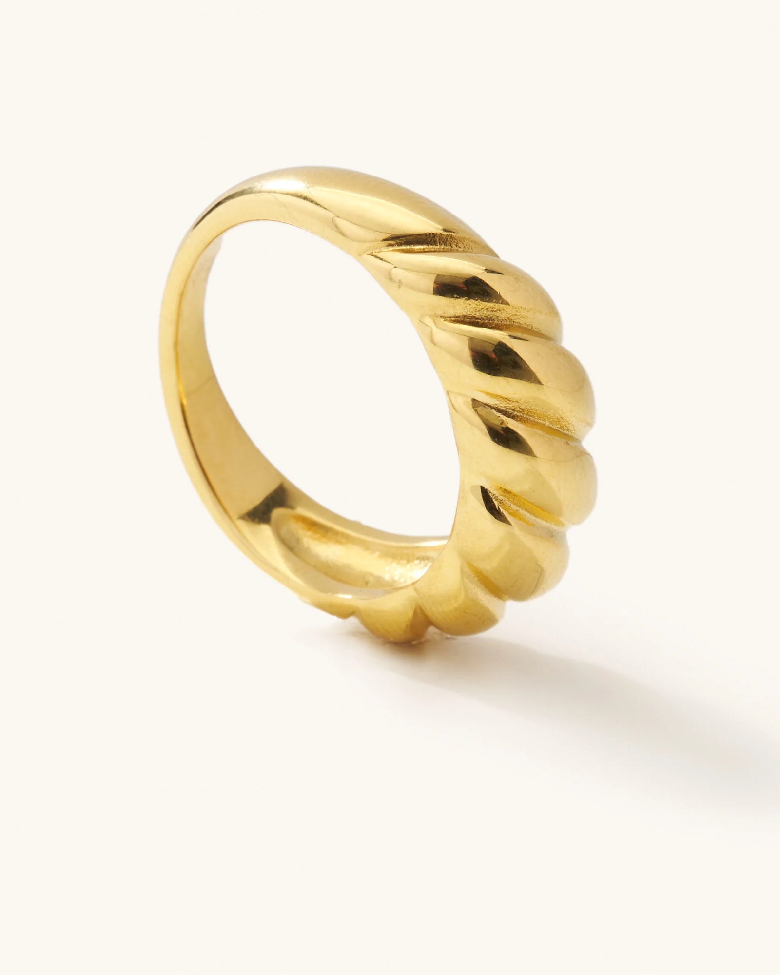 Gold ring with a twisted croissant design standing upright on a white background