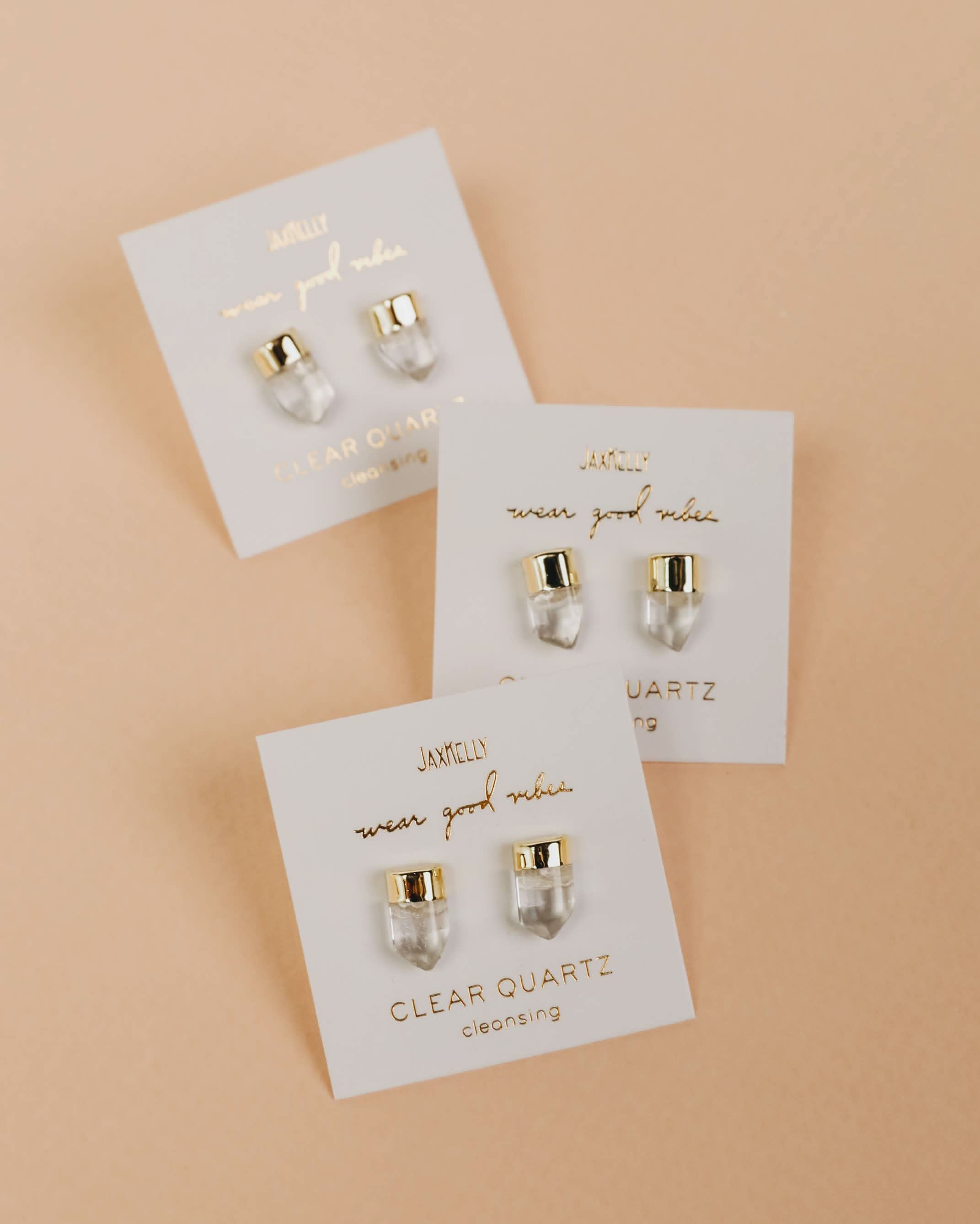Set of three pairs of earrings on white cards with gold accents against a beige background