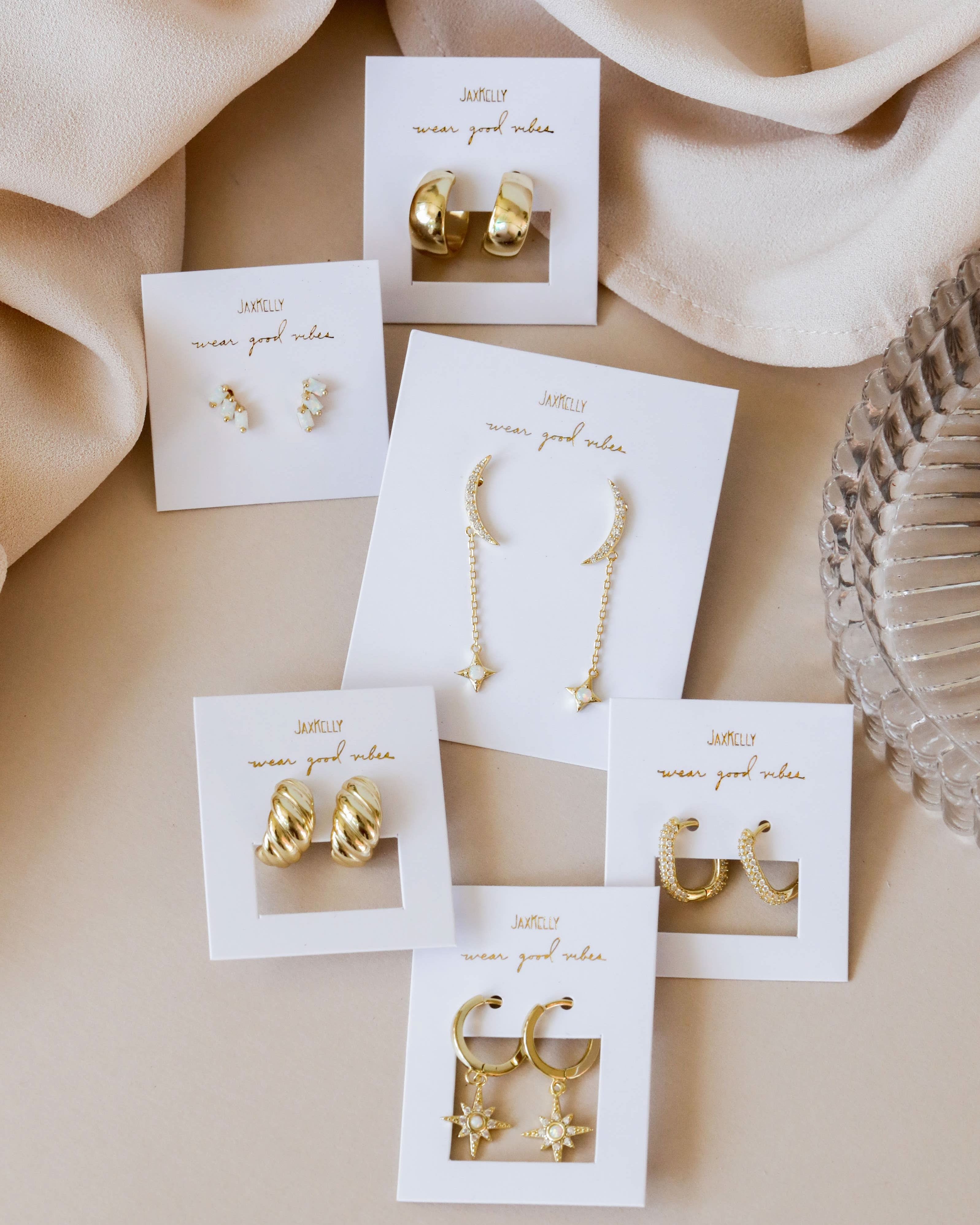 Set of gold earrings on white cards with 'nunun' branding against a beige fabric background.