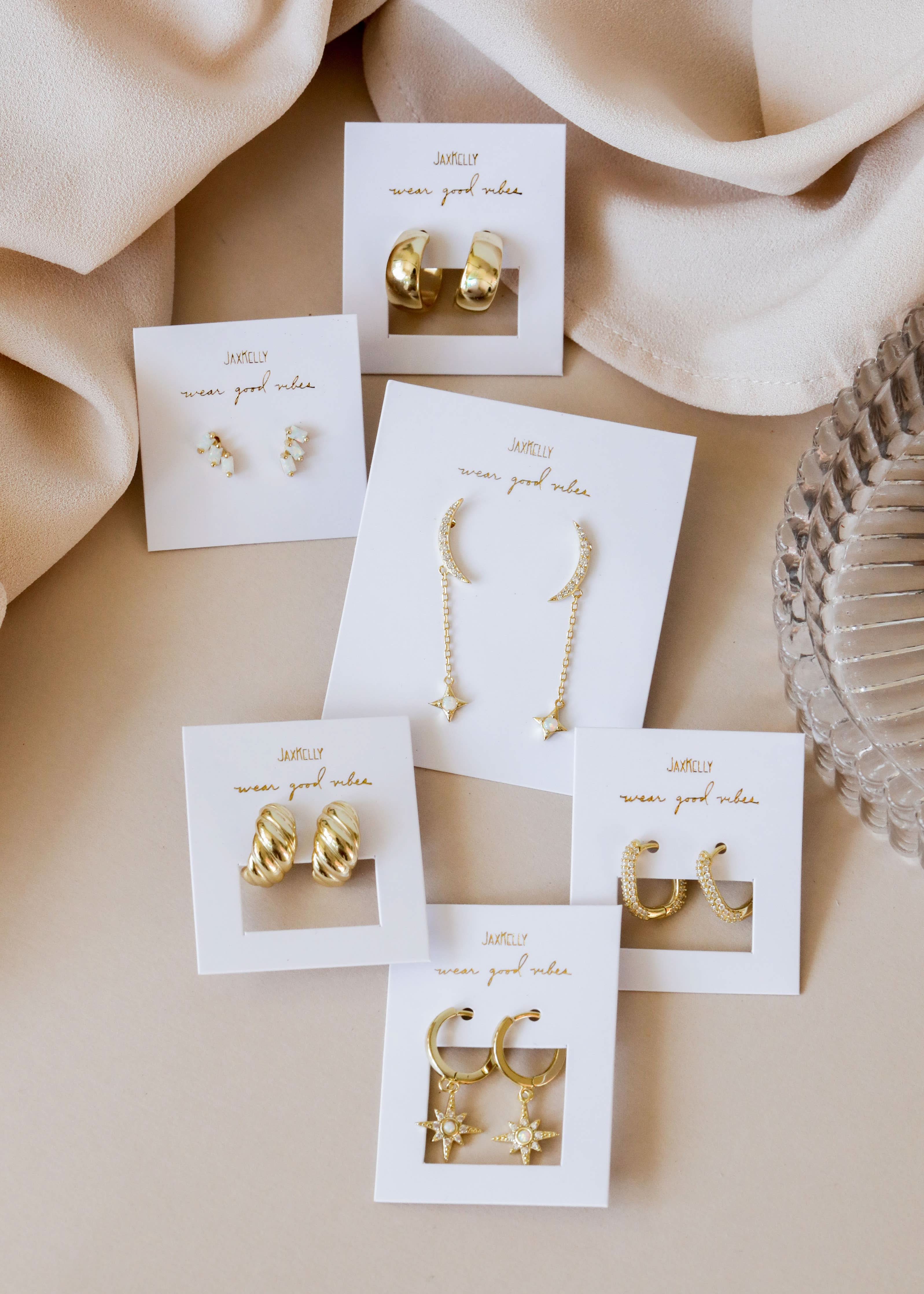 Set of gold earrings on white cards with 'nunun' branding against a beige fabric background.