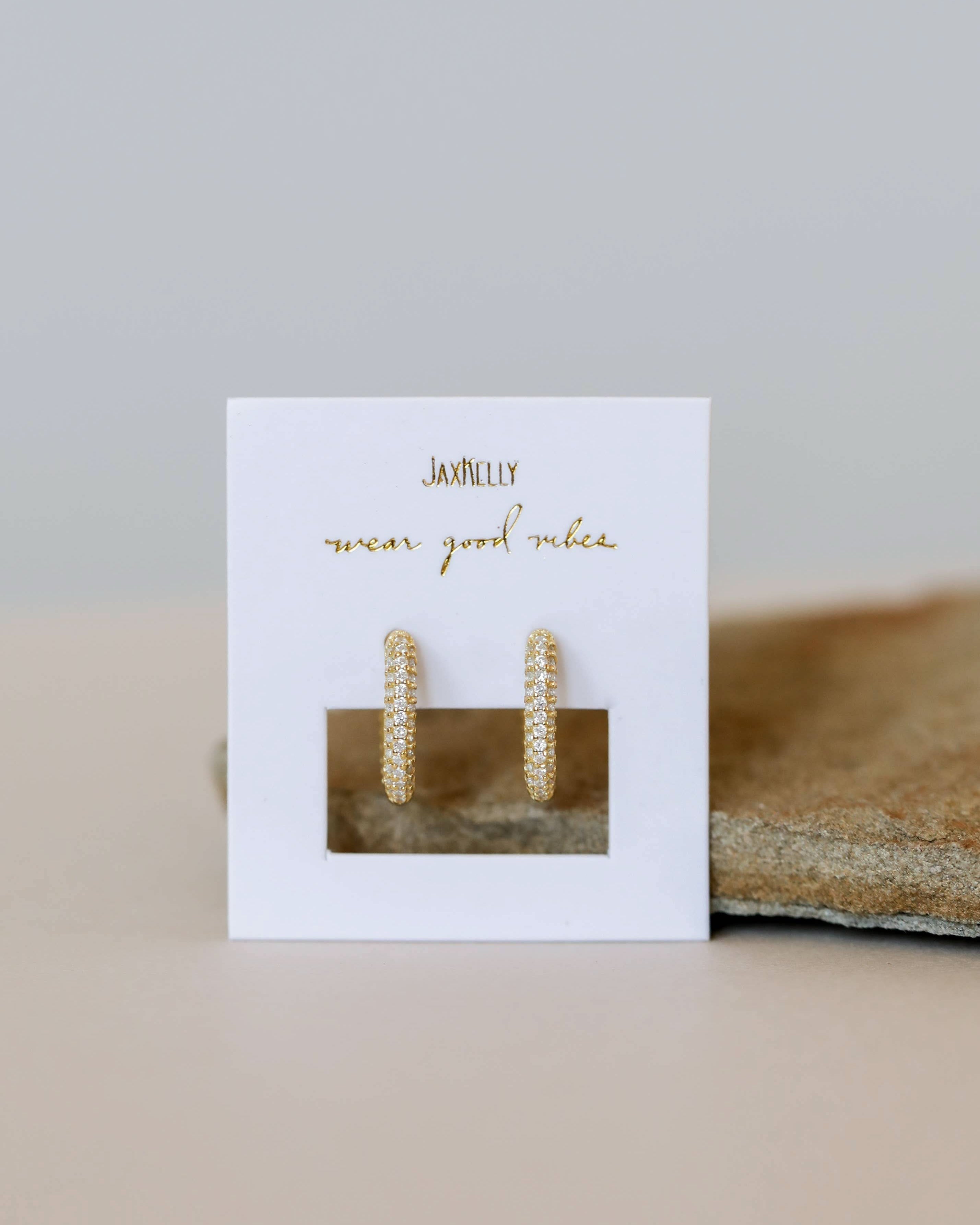 Gold hoop earrings on a white card with gold text, placed on a beige surface.