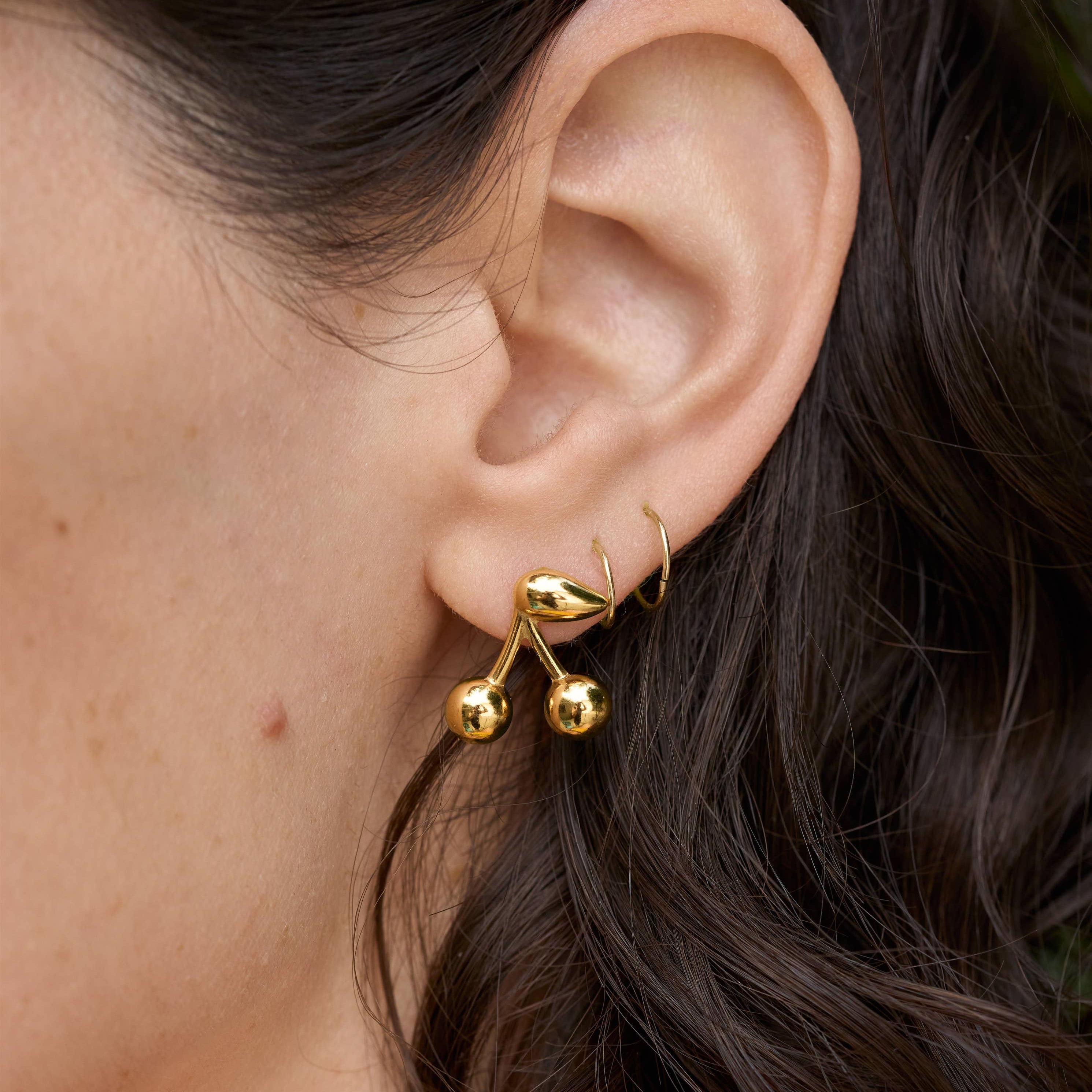 Gold Maraschino Studs Close-up of an ear wearing a gold earring with dark hair.