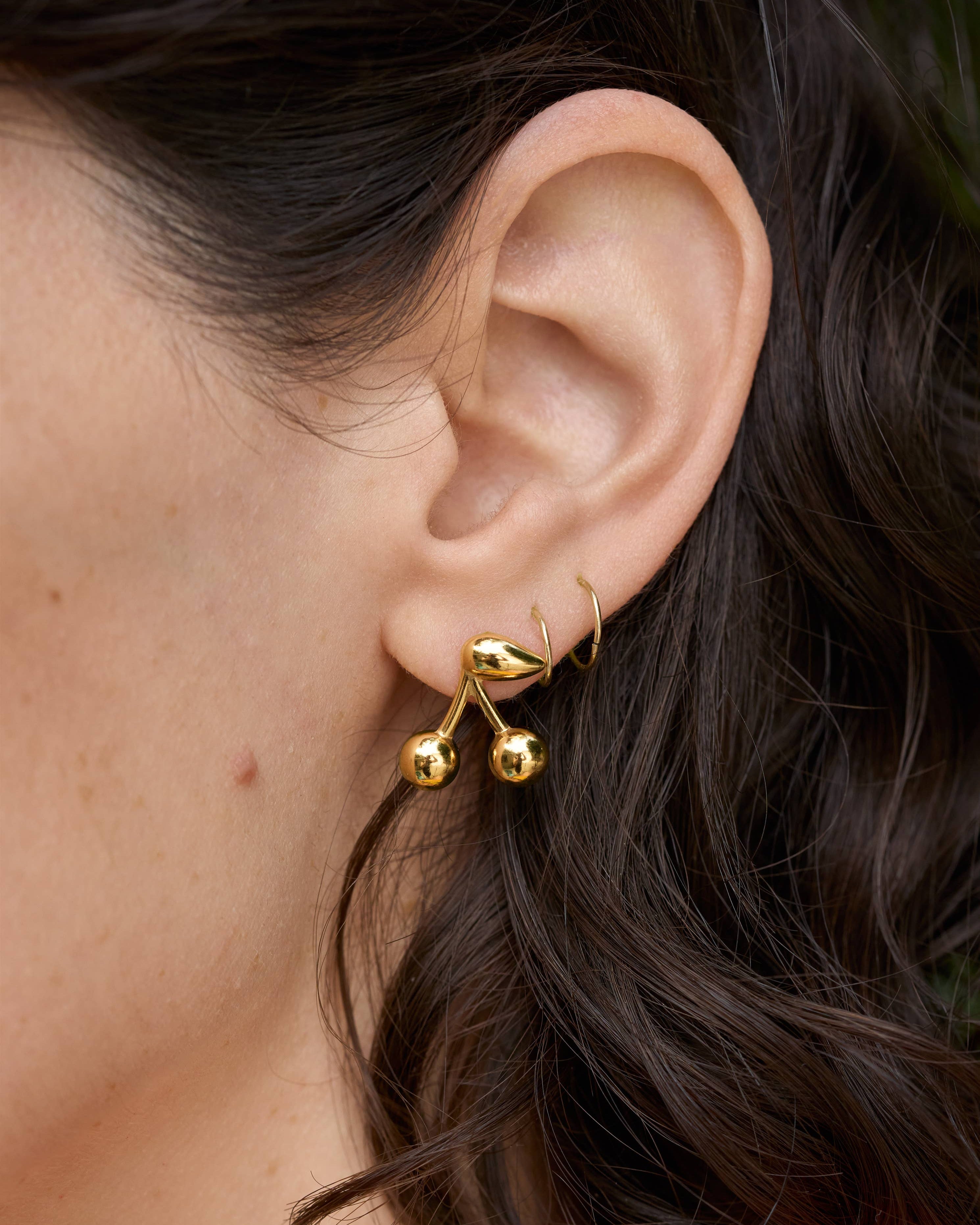 Gold Maraschino Studs Close-up of an ear wearing a gold earring with dark hair.
