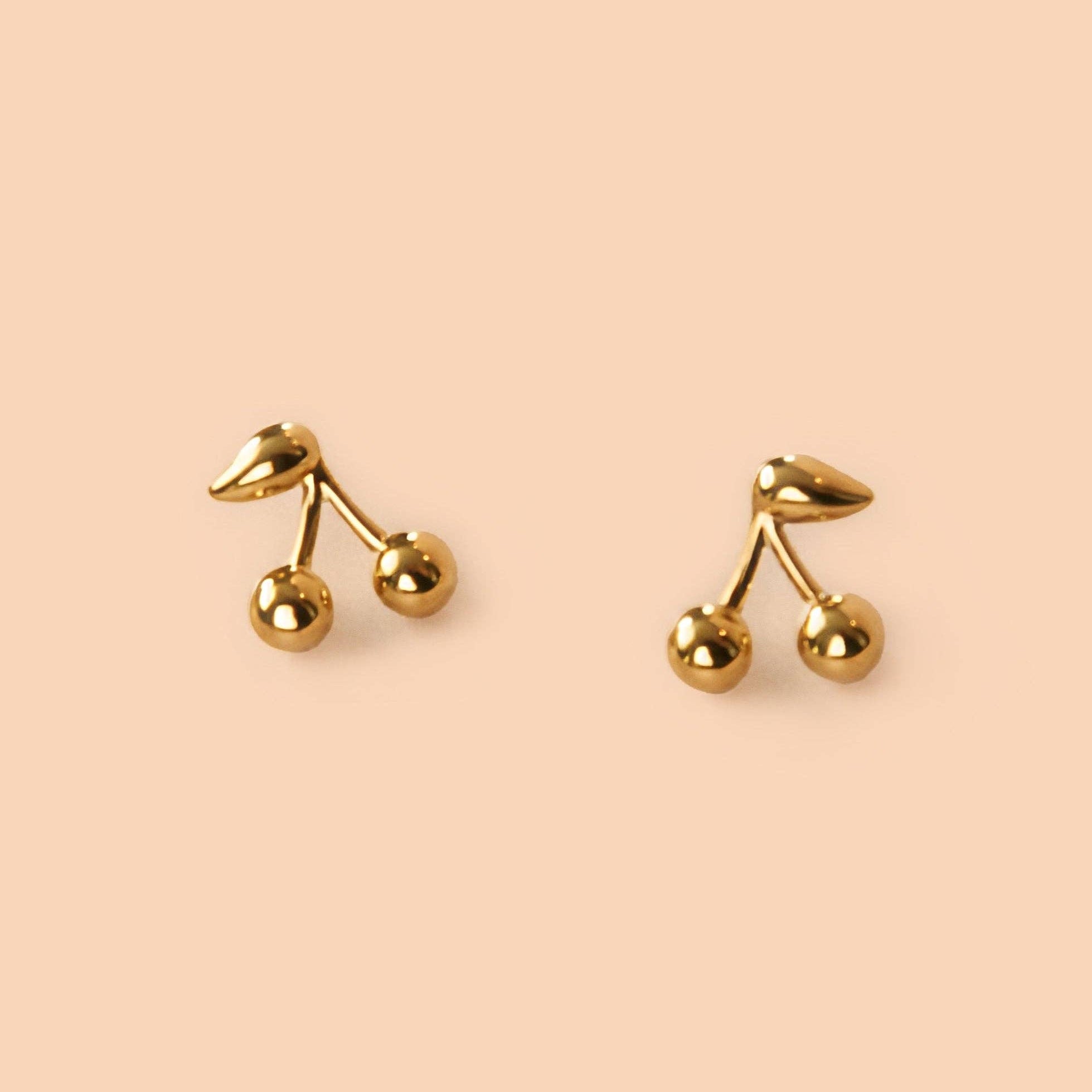 Maraschino Studs Gold cherry-shaped earrings on a beige background