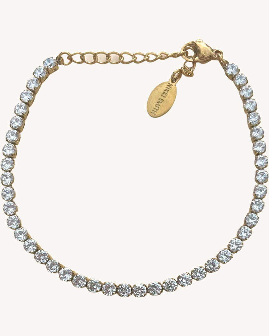 Dainty gold shimmer tennis bracelet laying on a white background