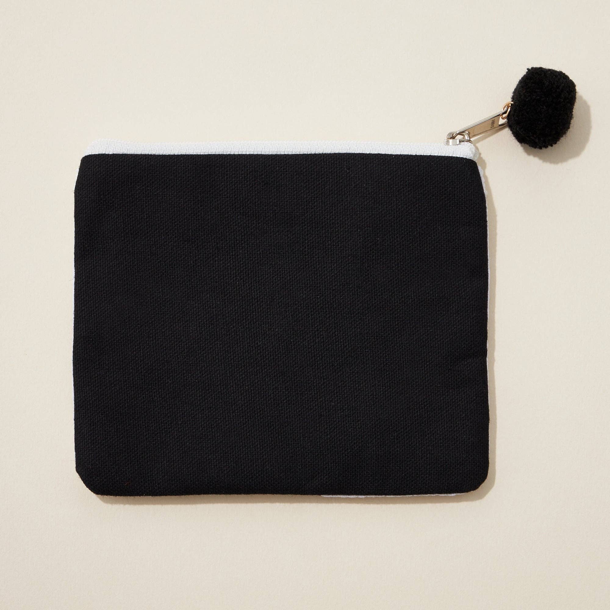 Black pouch with a pom-pom on a beige background