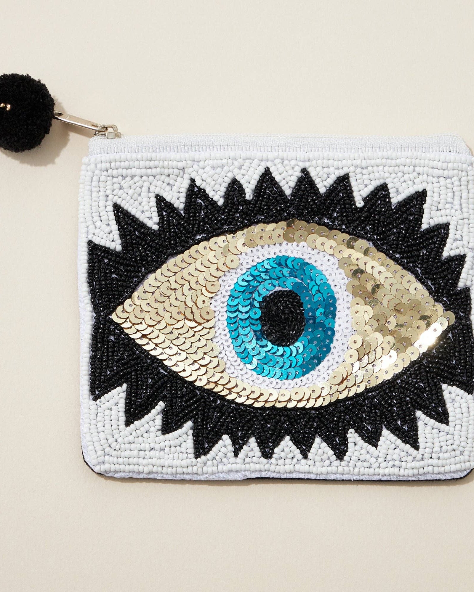 Pouch with eye design featuring sequins on a beige background