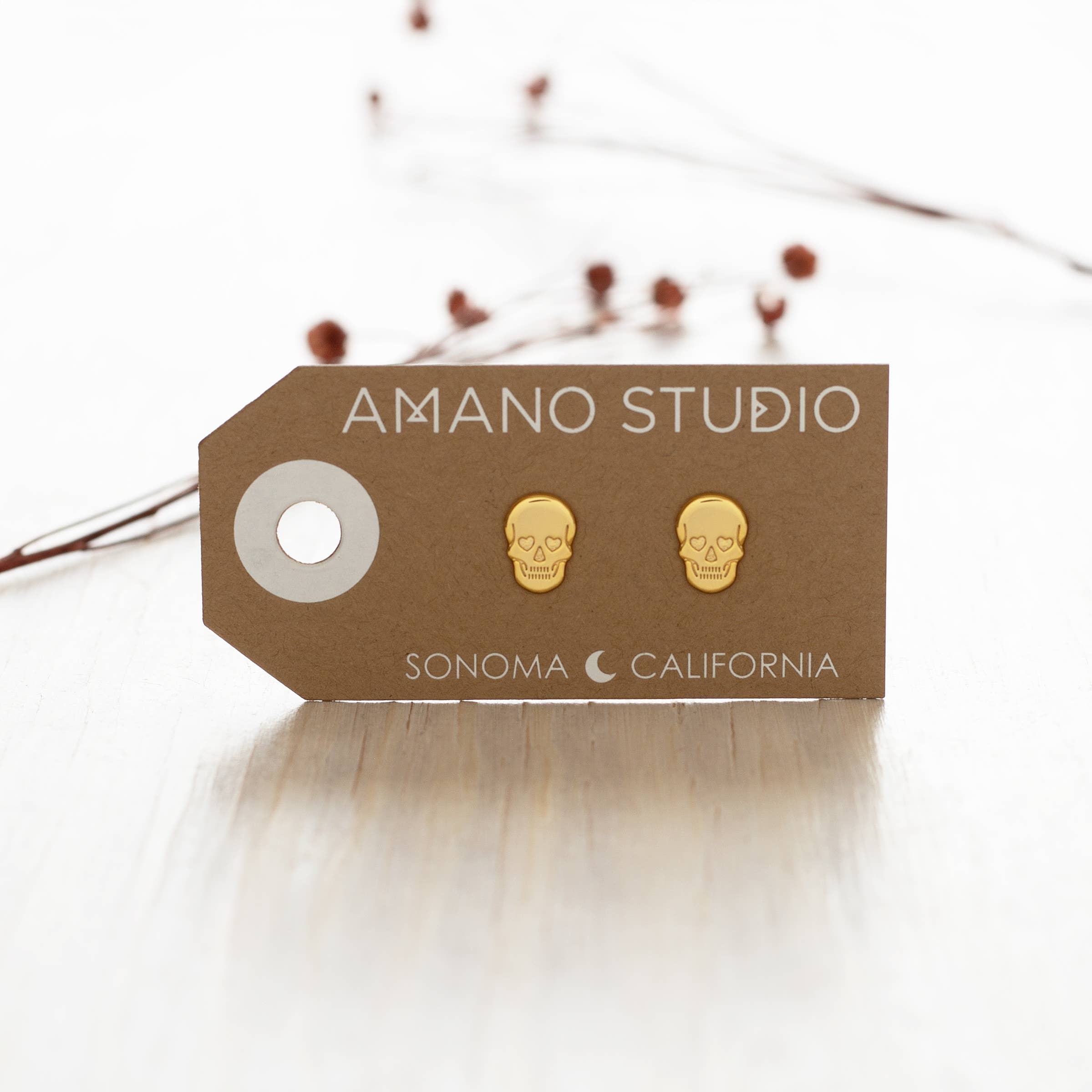 Gold skull earrings on a 'Amano Studio' branded card